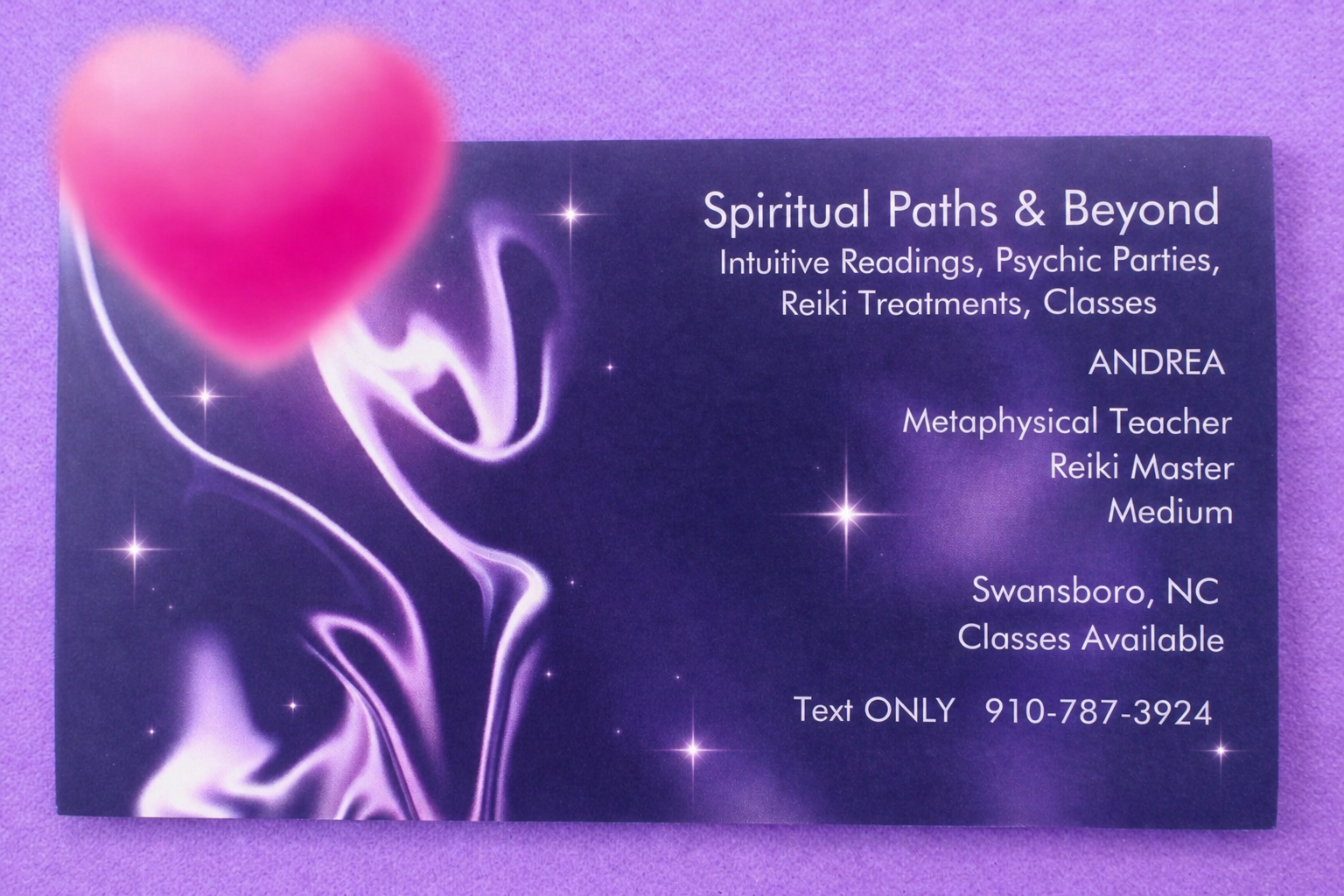 A business card with a purple and black cosmic background and a pink heart-shaped balloon in the top left corner. The card contains information about spiritual paths, intuitive readings, psychic parties, Reiki treatments, classes, and features contact details for Andrea, a metaphysical teacher and Reiki master in Swansboro, NC.