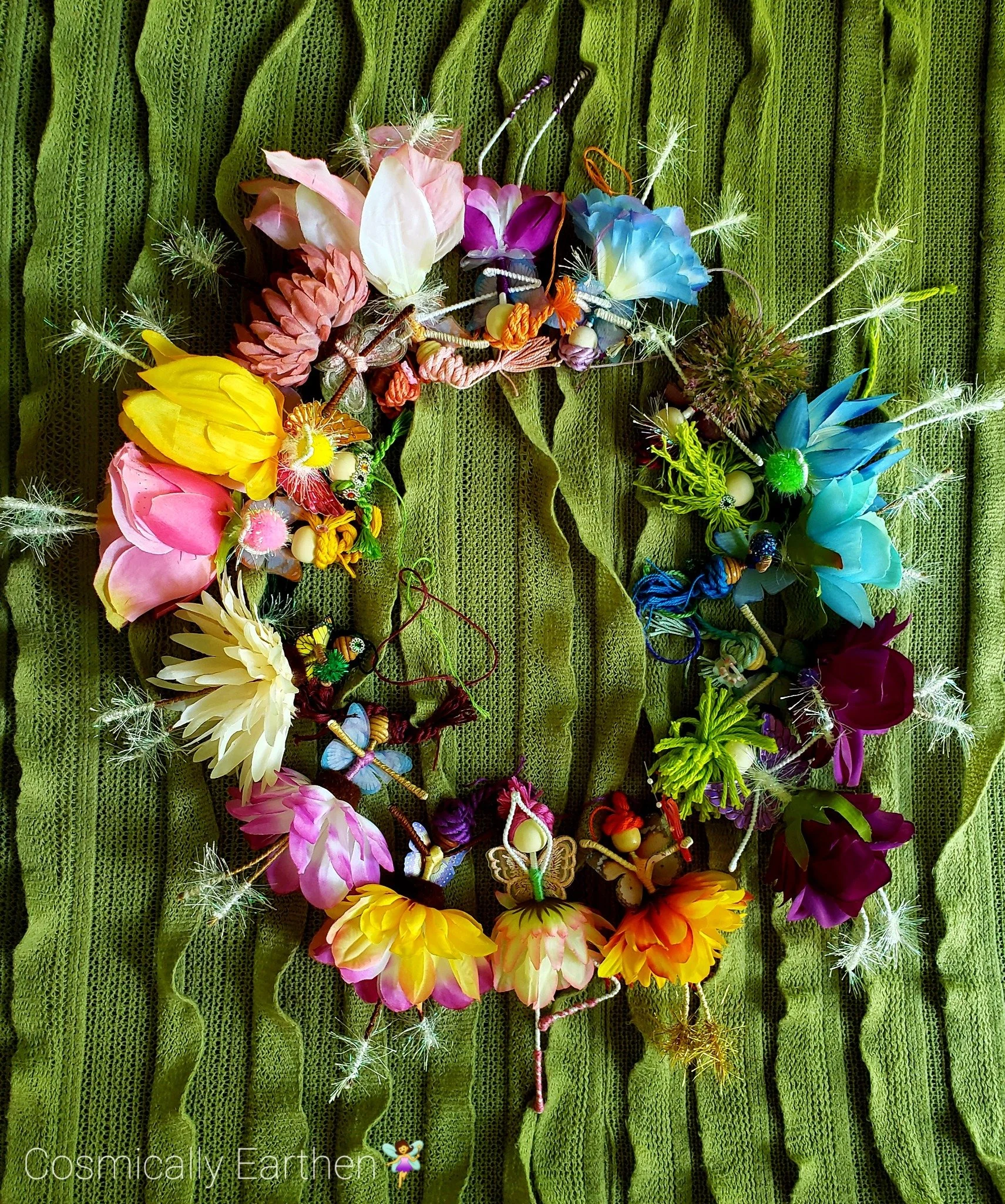 Colorful handmade Petal Keeper flower fairies arranged in a circle on green fabric, showing their varied flowers, wings, yarn hair, and botanical details.