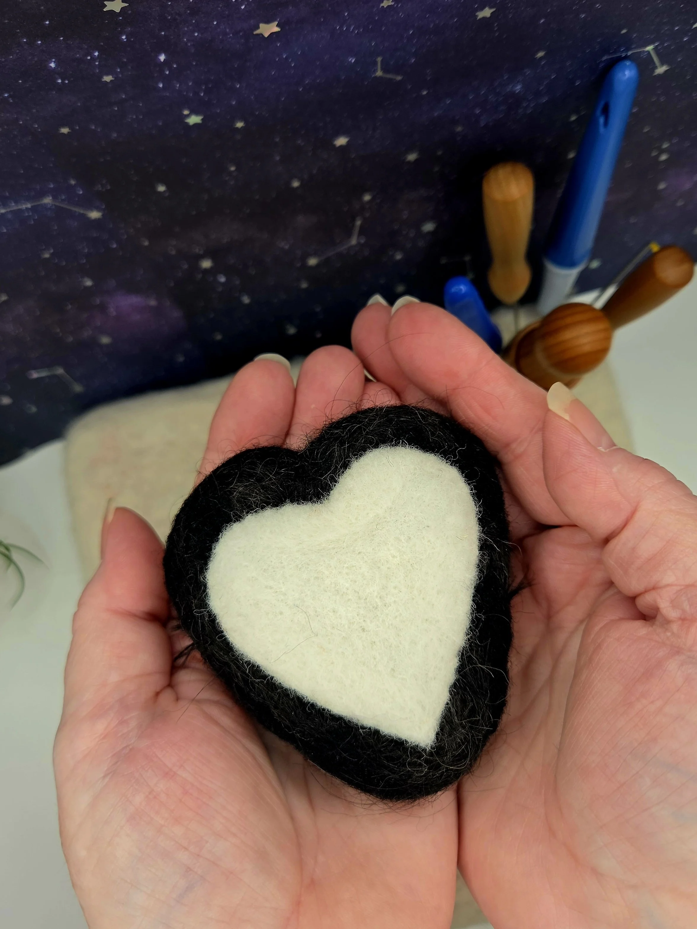 A person holding a felt heart with a black border and a white interior.