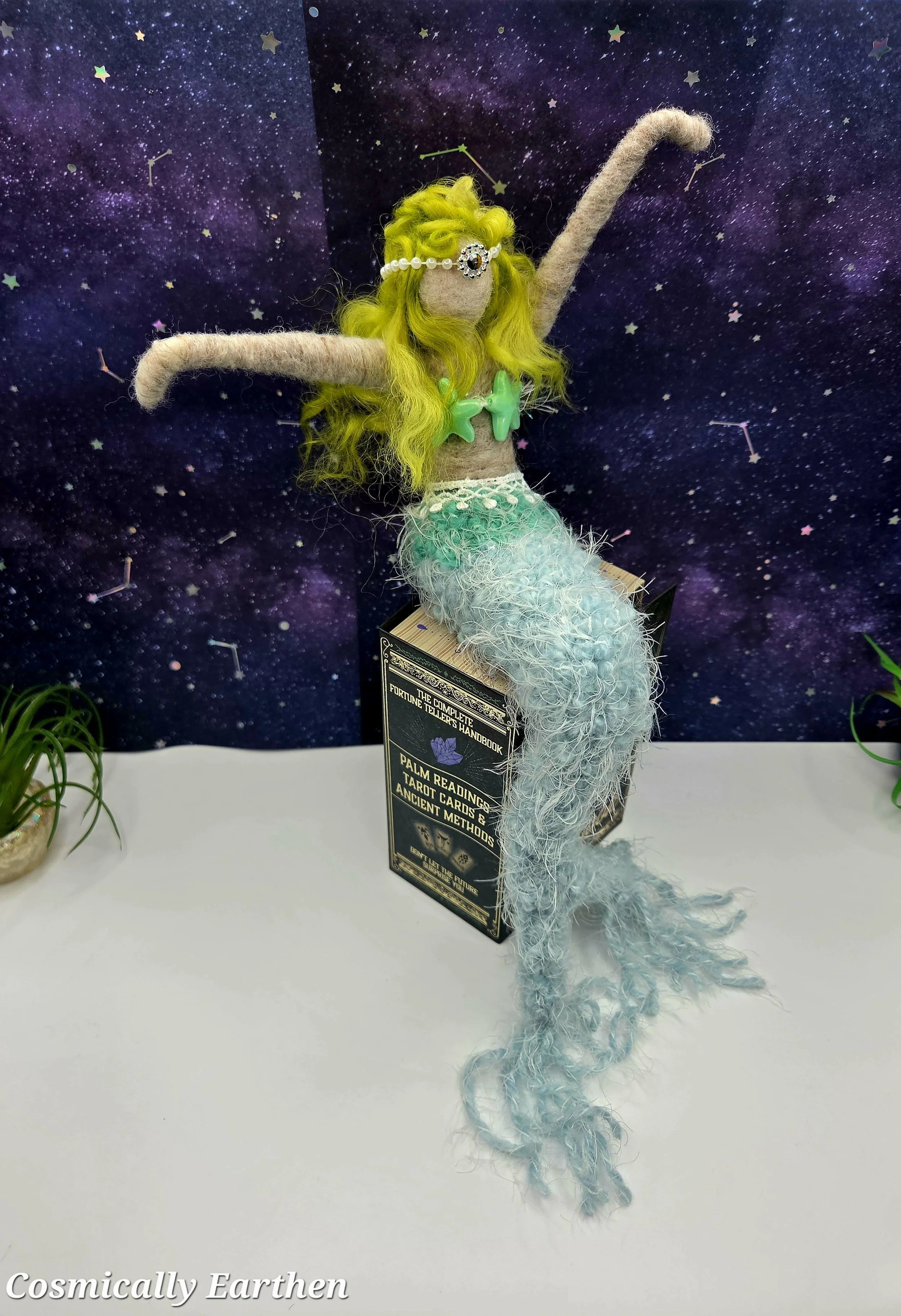 OOAK mermaid doll sitting on book with draping tail, detailed wool fibers and coastal decor including starfish and galaxy background