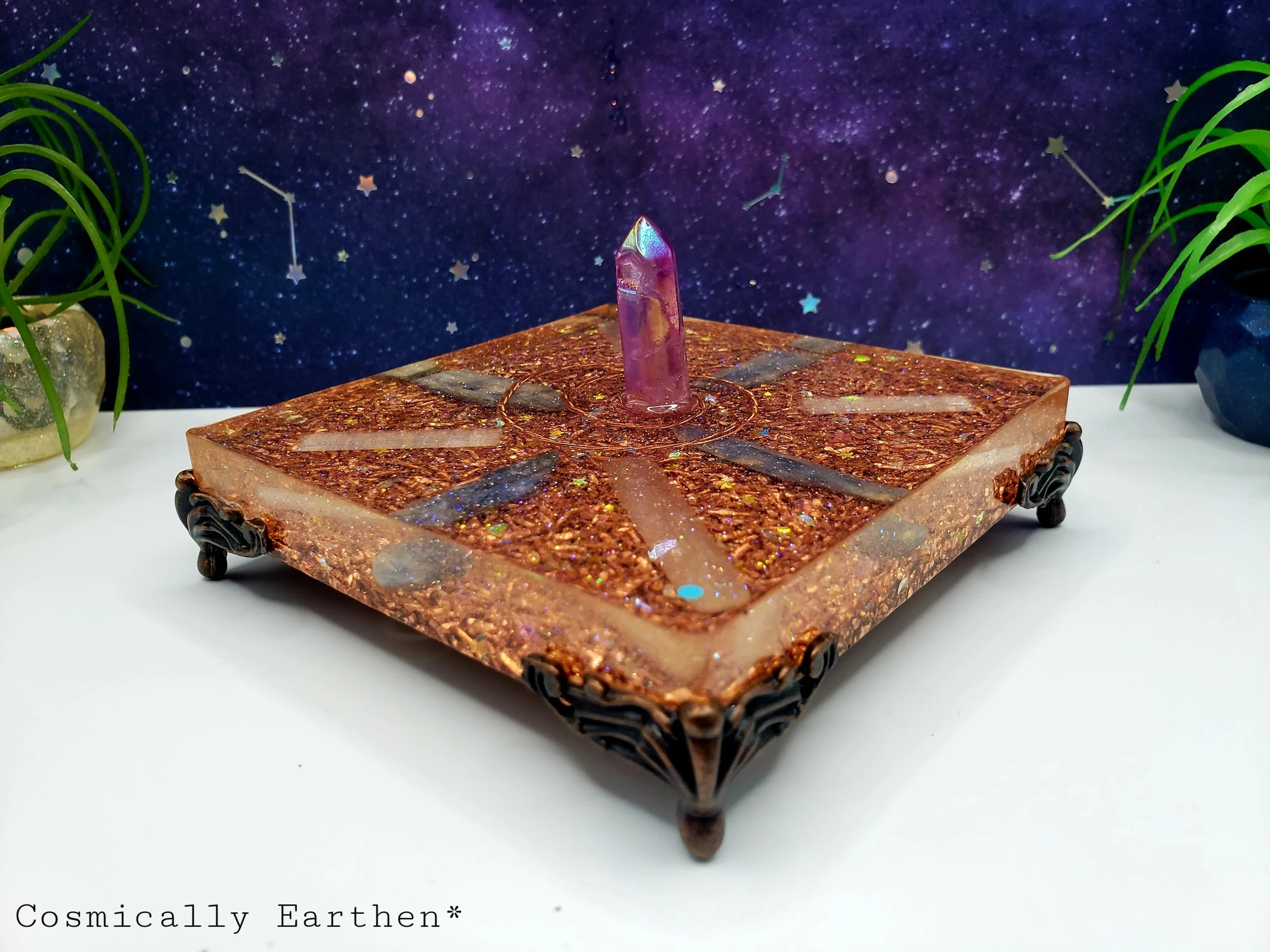 A decorative item resembling a spaceship or crystal on an ornate square base with a starry, cosmic background and potted plants on either side.