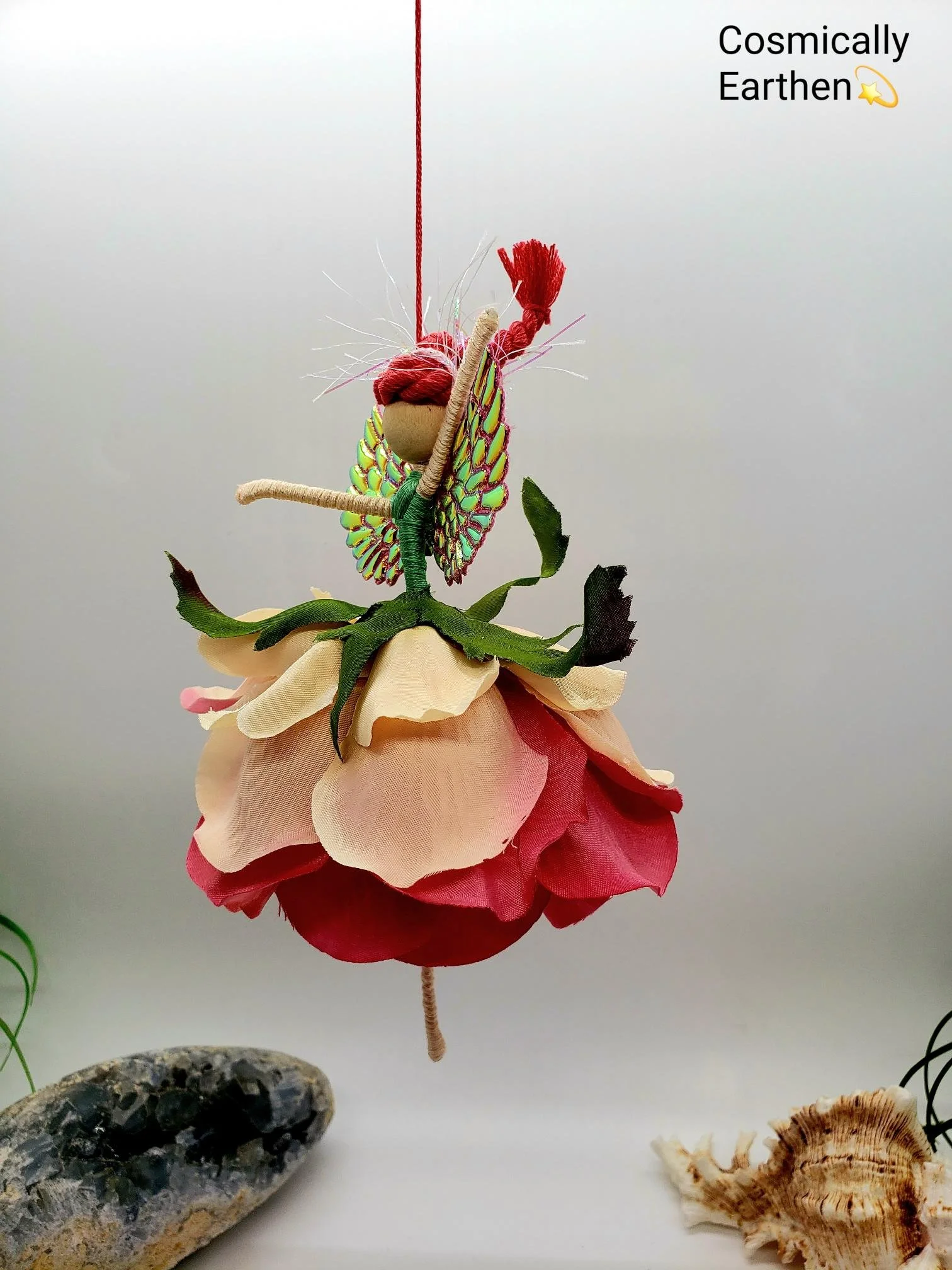 A handmade decorative art piece resembling a butterfly perched on a flower, with natural rocks and seashells nearby.