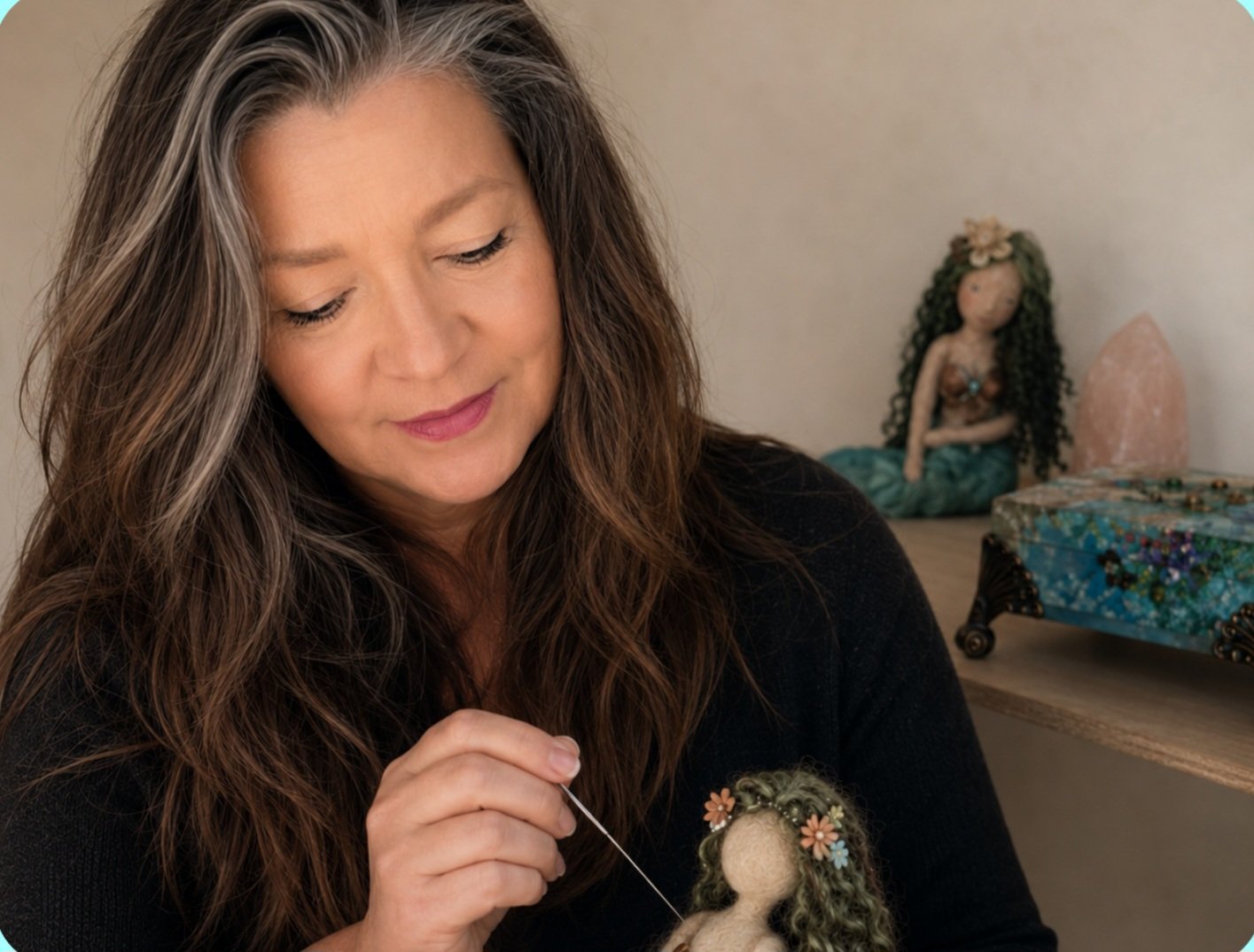 A woman with long wavy brown hair, wearing a black sweater, is sewing a doll with curly green hair and floral accessories in her right hand. She is focused on her work, and in the background, there is a figurine of a mermaid with long black curly hair and a seashell top, along with a salt lamp and a decorative box with jewelry.