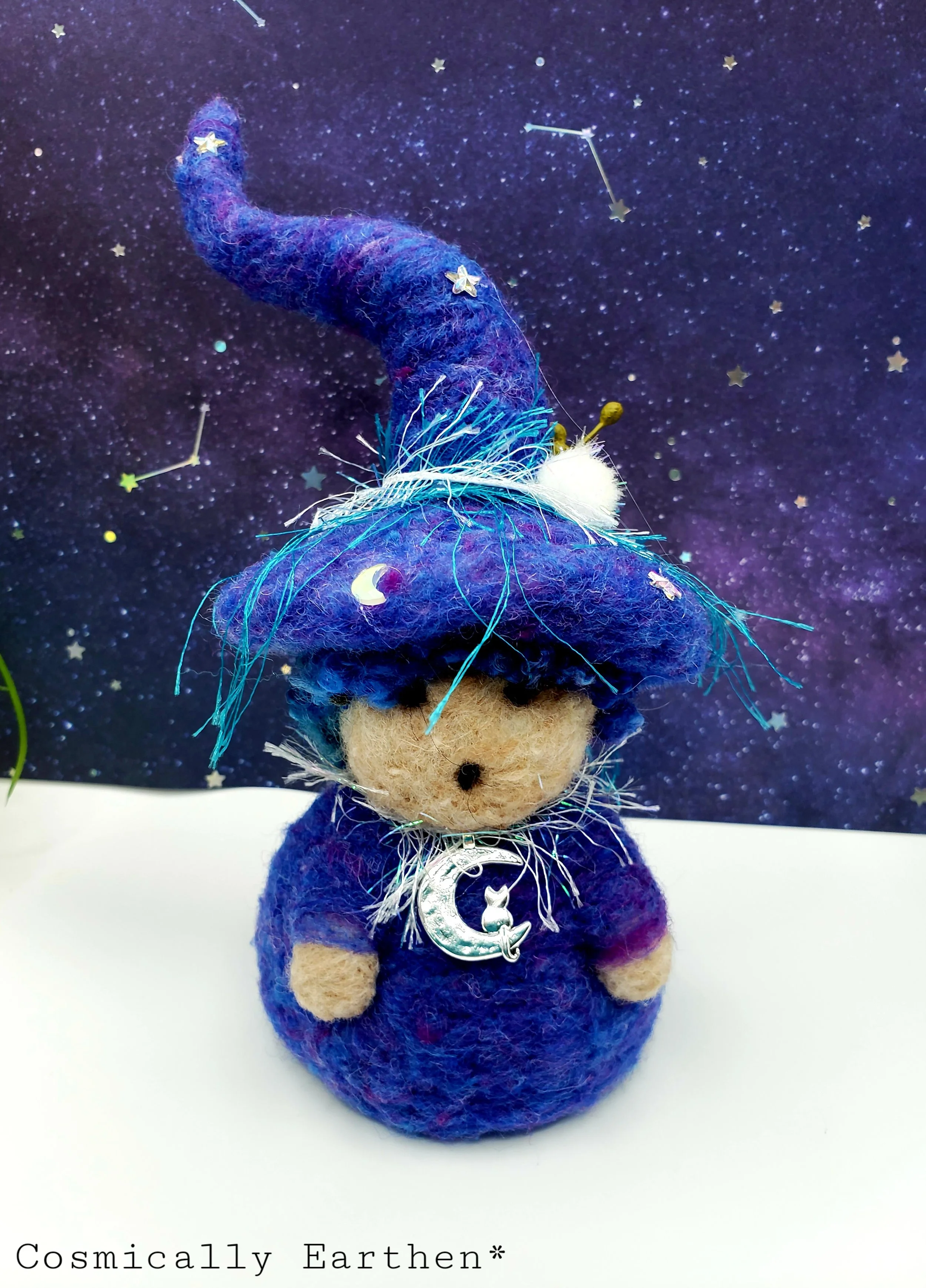 Needle-felted Groundling trio with blue, black, and green hats, adorned with flowers, crystals, and charms, set against a starry background with small green plants.