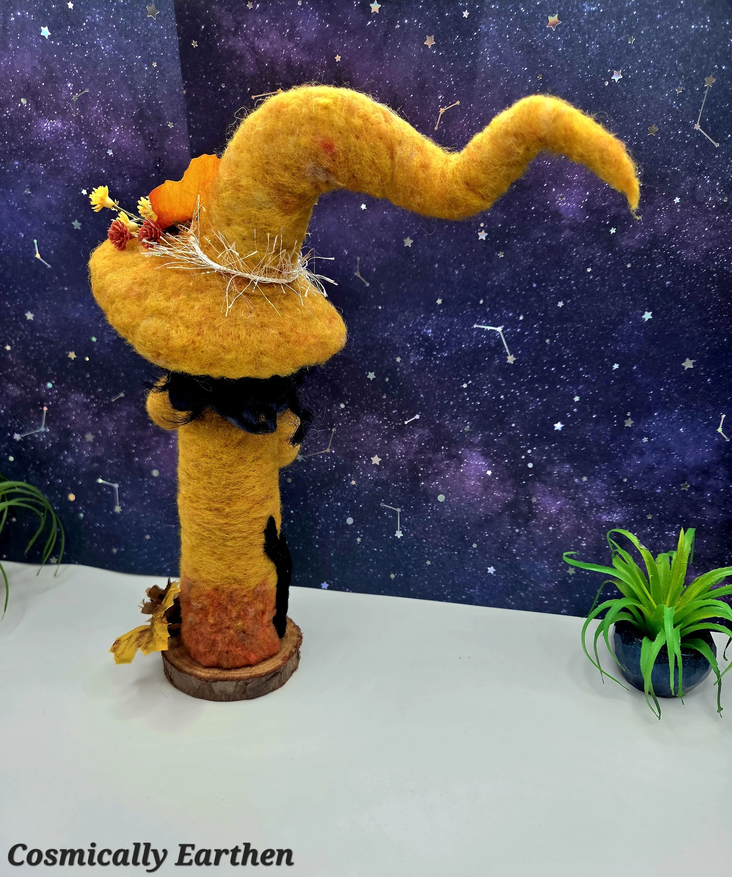 Back view of needle felted autumn witch doll Marigolde with textured wool fibers and curved hat, mounted on a natural wood base as a one-of-a-kind handmade art doll