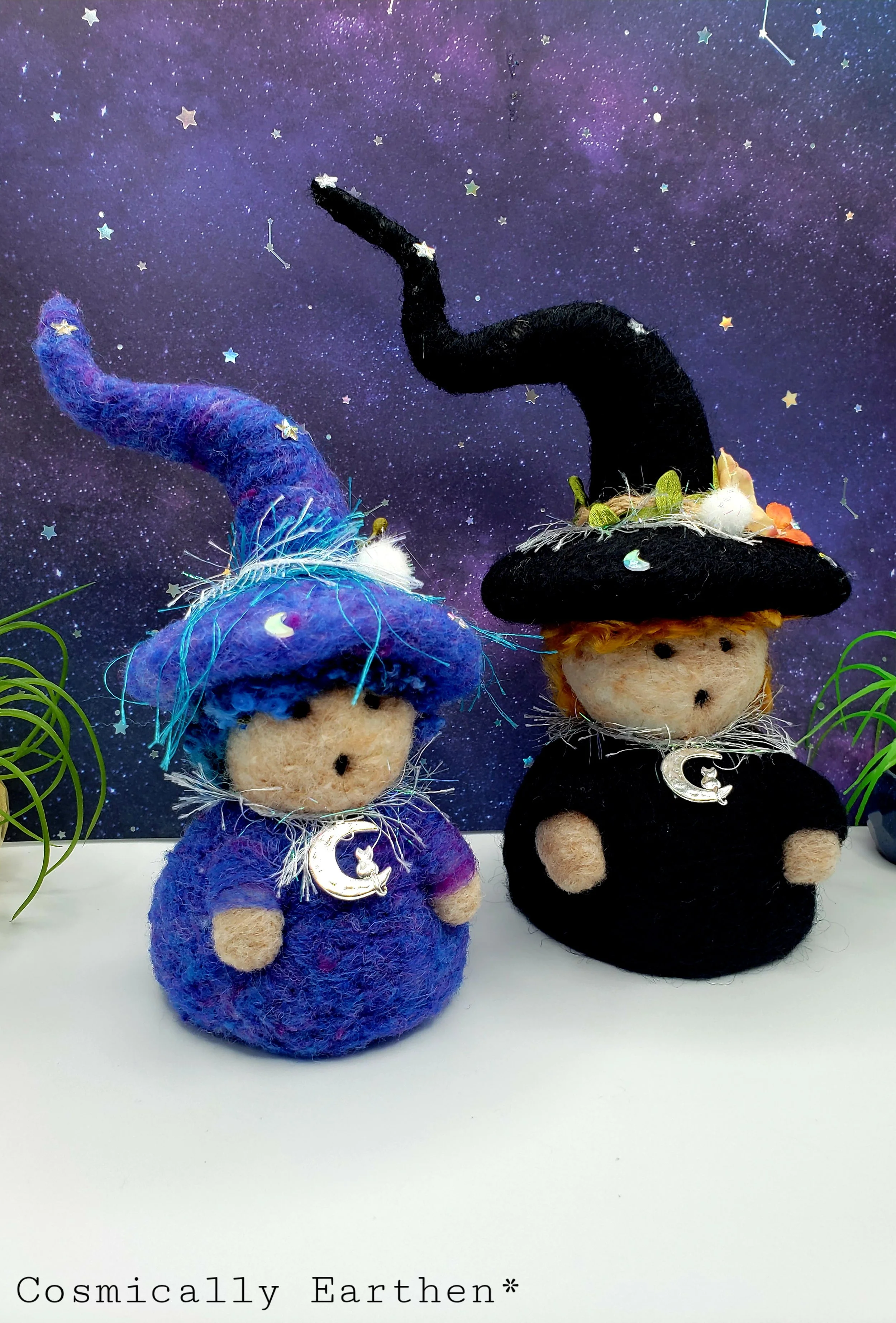 Needle-felted Groundling trio with blue, black, and green hats, adorned with flowers, crystals, and charms, set against a starry background with small green plants.