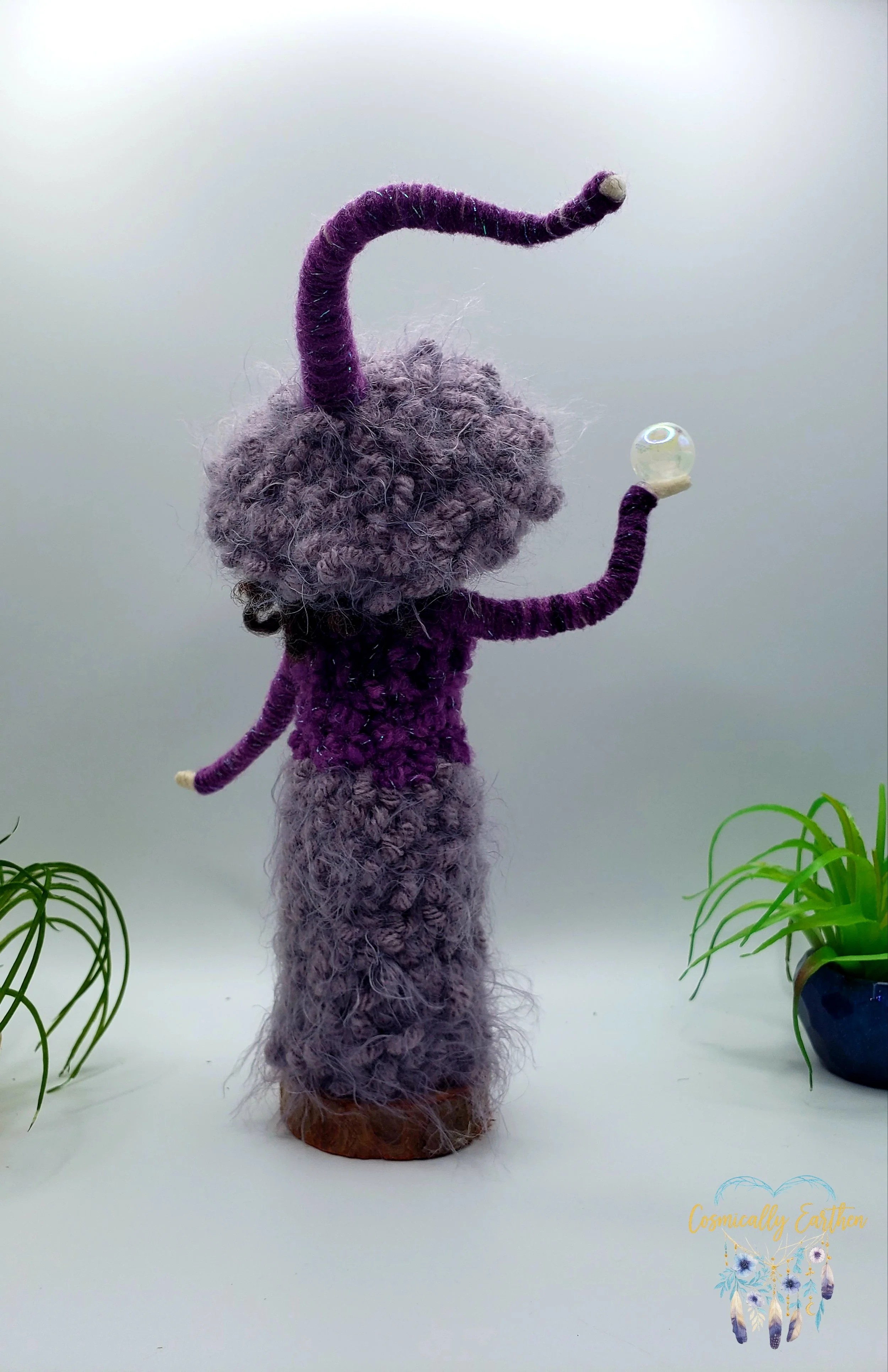 Back view of needle felted purple doll Velora with layered wool fibers and pointed hat, mounted on a natural wood base as a one-of-a-kind handmade art doll