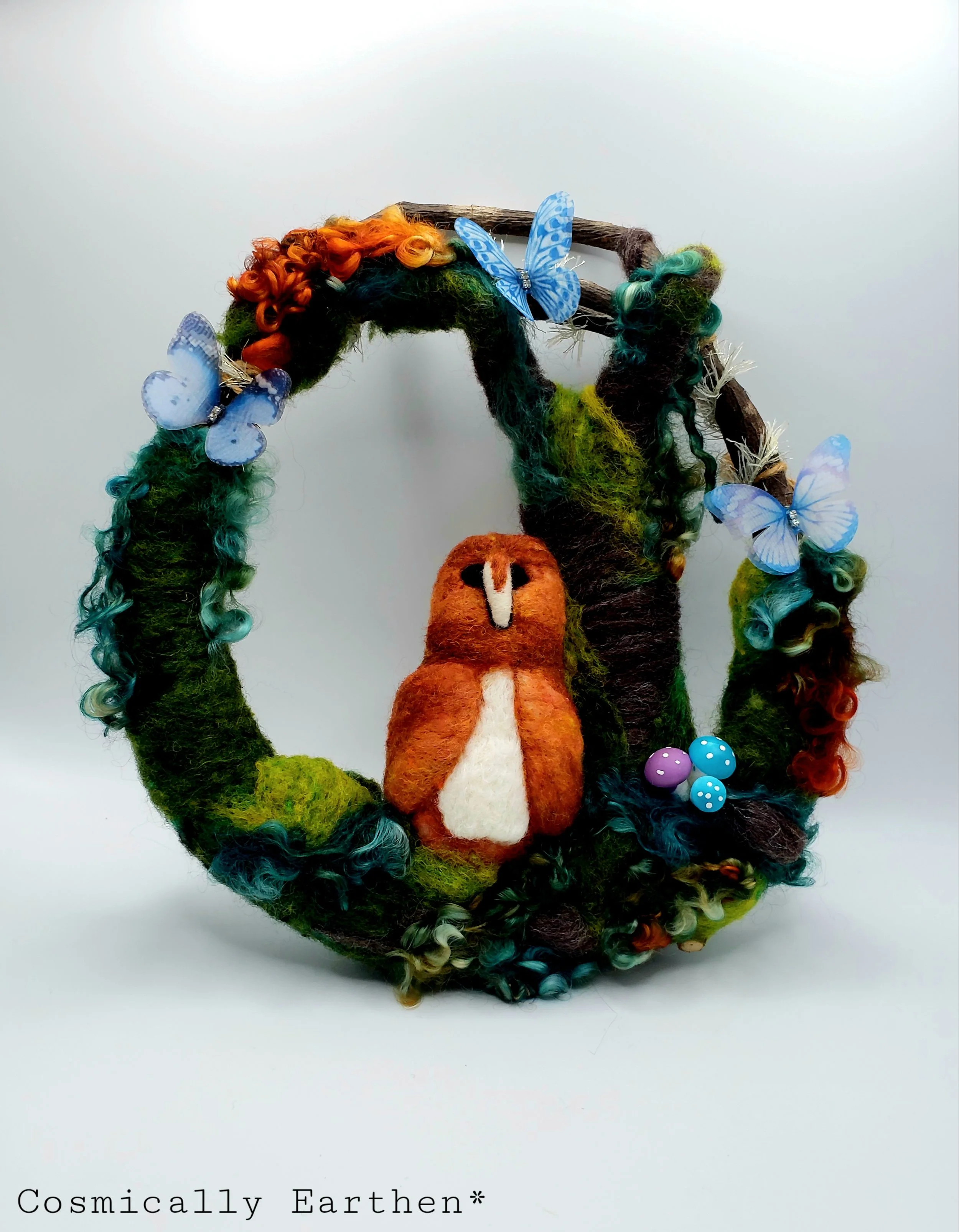 Handcrafted needle-felted wreath featuring a barn owl, blue butterflies, and vibrant mossy textures. A magical forest altar piece by DeAn’Na.