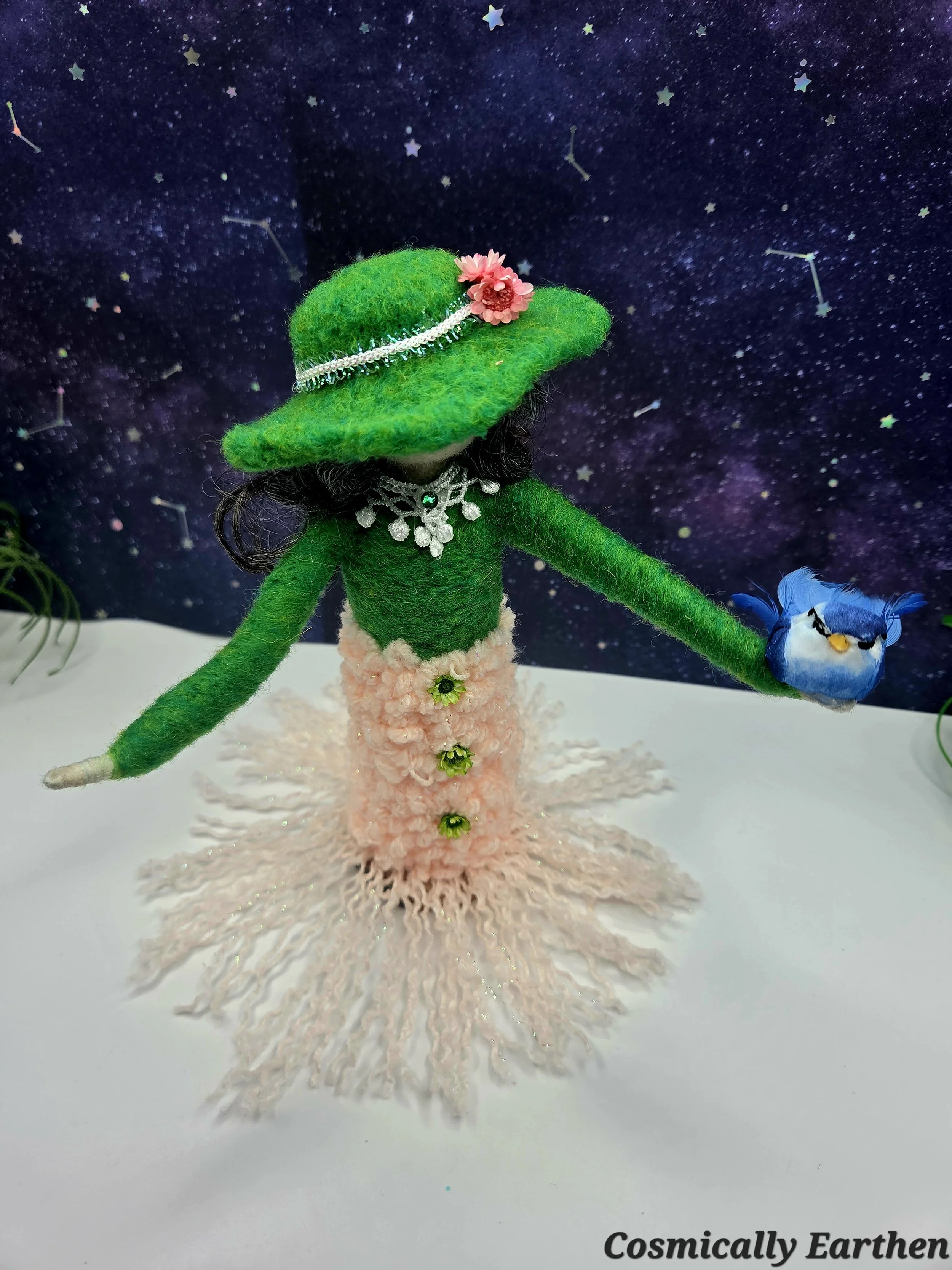 Close-up of needle felted art doll Liora in green tones holding a bird, showing detailed wool textures and handcrafted fiber art features