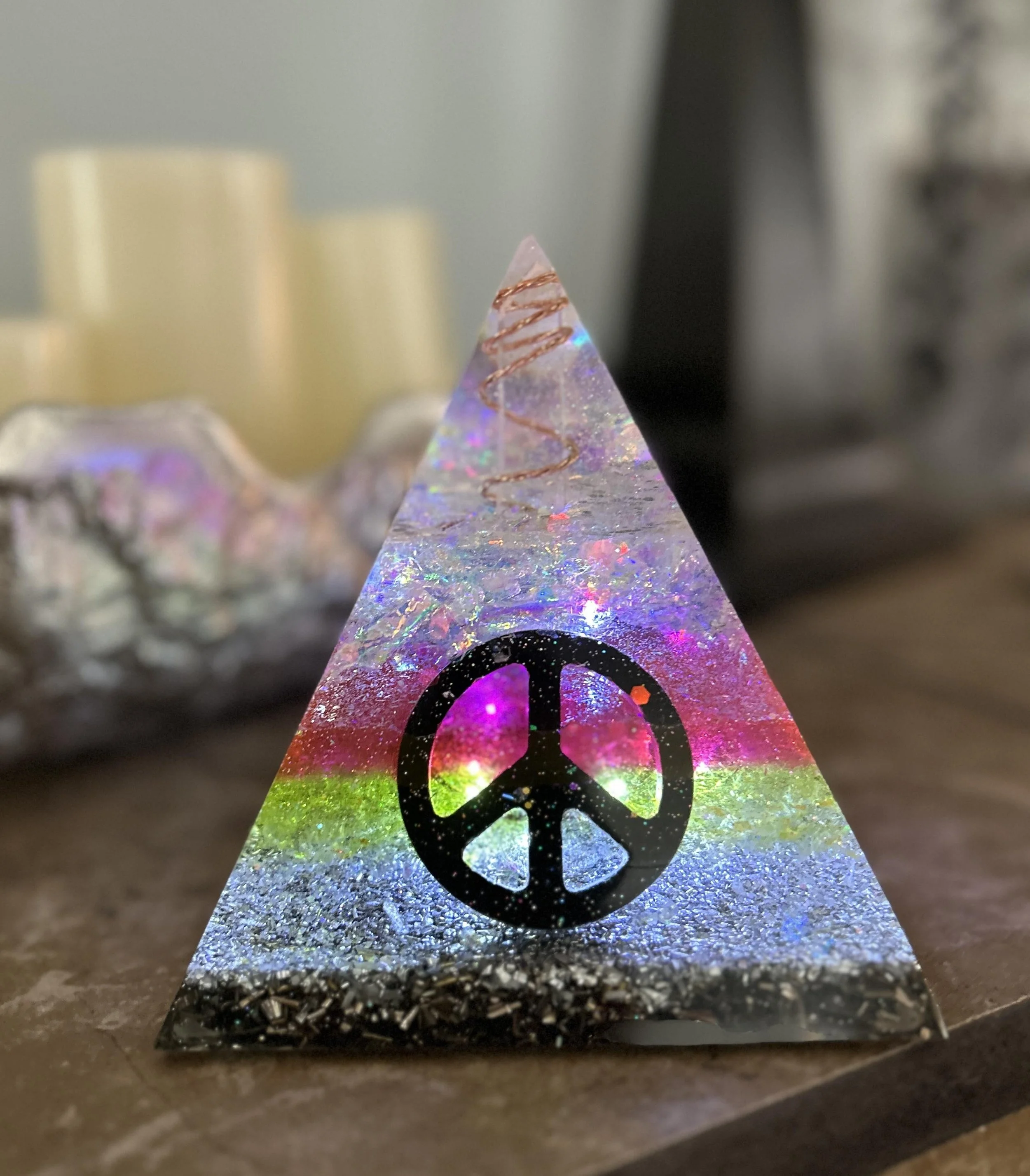 Close-up view of a small iridescent crystal mountain with a black peace symbol design on its front, set on a glittery surface.