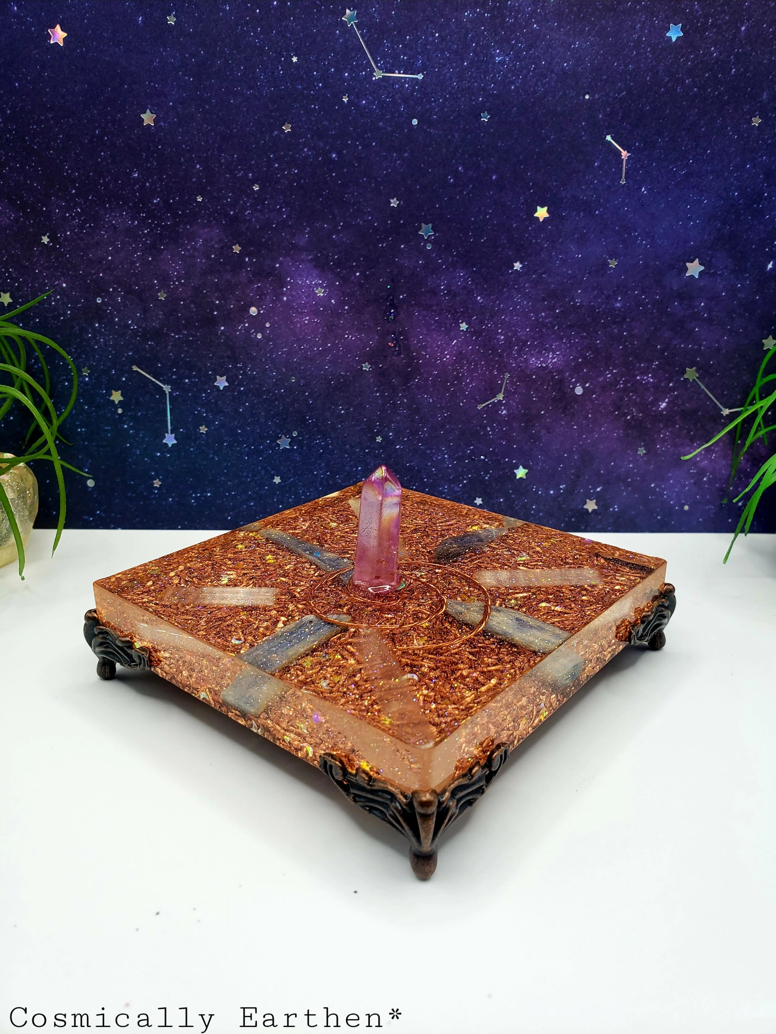 Side view of orgonite crystal charger with cosmic background, showing decorative feet and central quartz point.