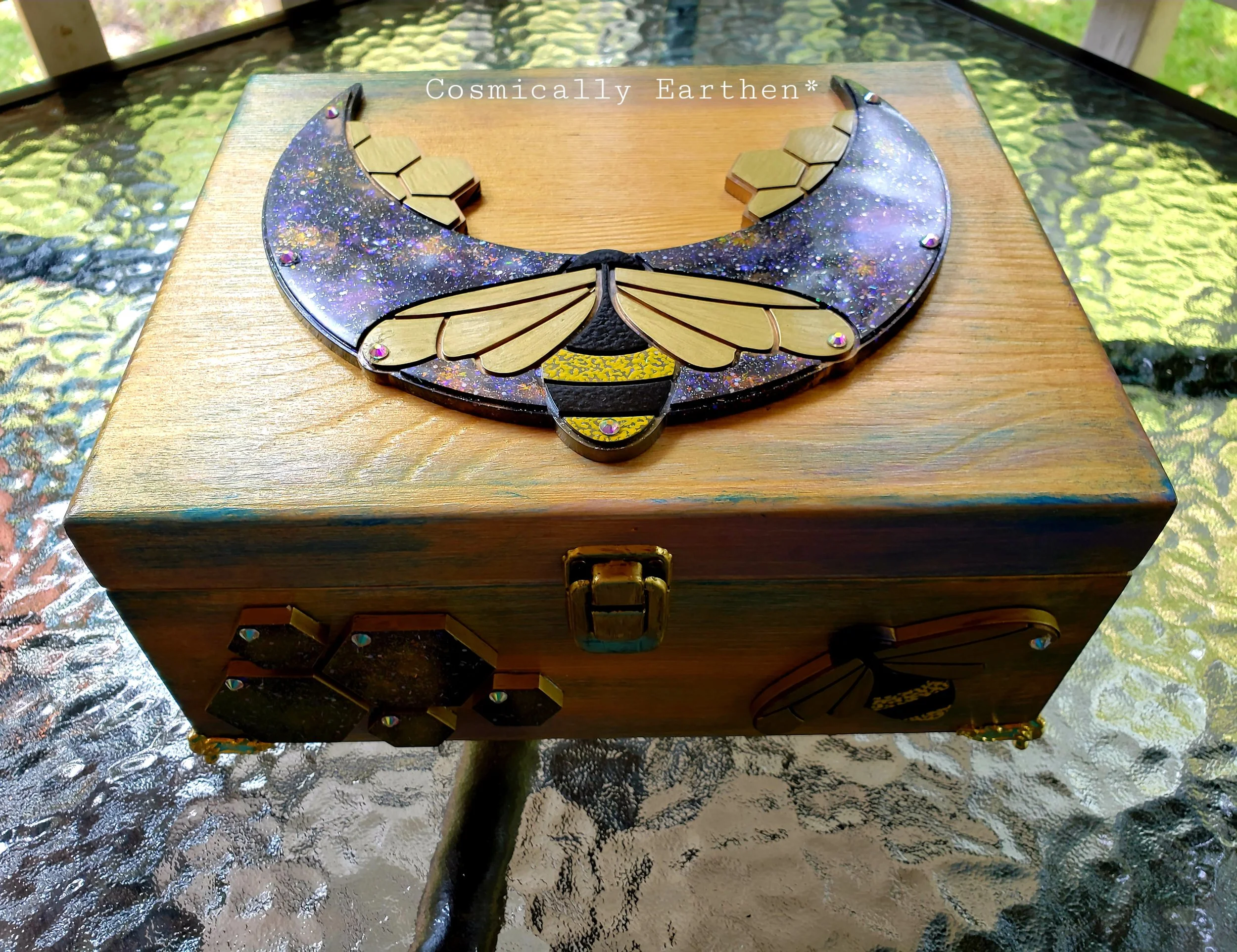 Decorative moon-shaped jewelry display with gold hexagonal pieces and butterfly wings design, resting on a wooden box, outdoors.