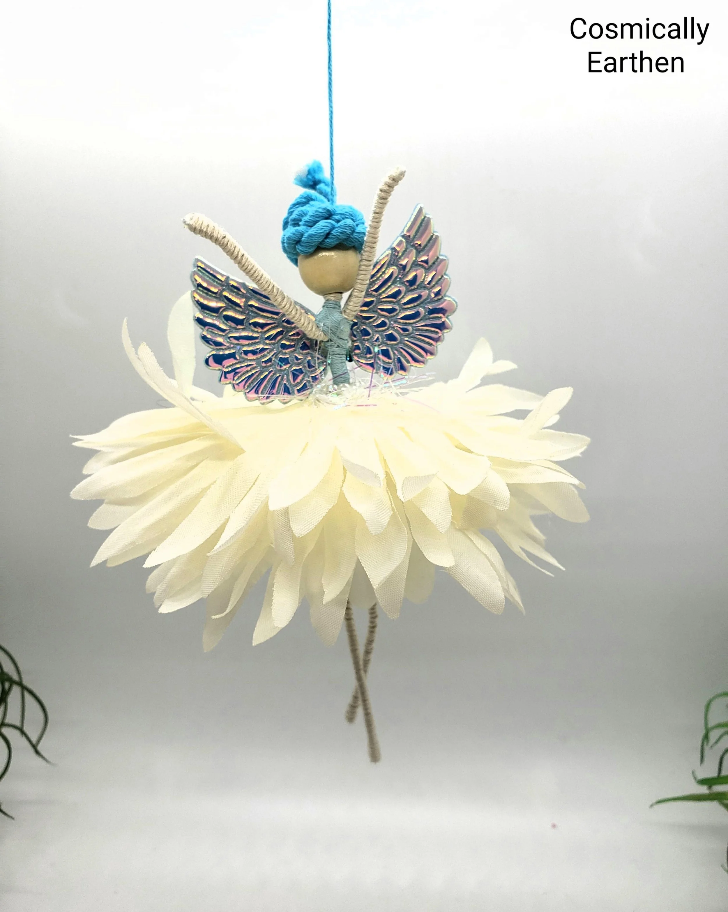 A decorative artificial flower with a cream-colored daisy-like blossom, a beige and iridescent butterfly-shaped embellishment, and a cluster of blue yarn resembling a bud, on a plain white background.