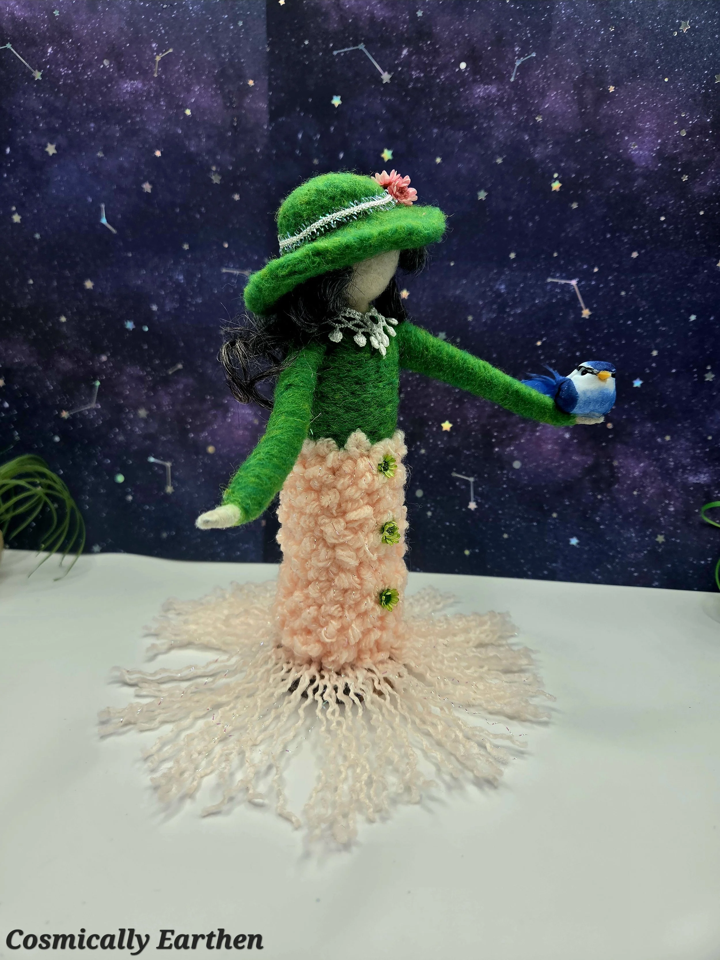 Side view of handmade needle felted doll Liora with textured green clothing and bird companion, mounted on a wood base as a collectible fiber art sculpture