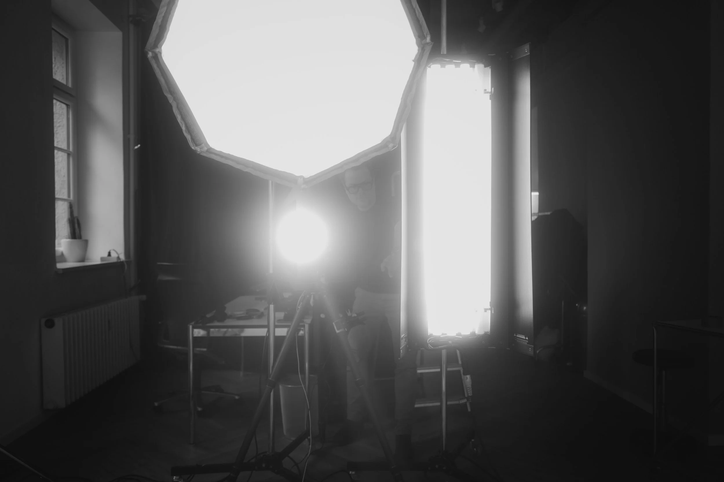A person setting up cameras and lighting in a room with a window.