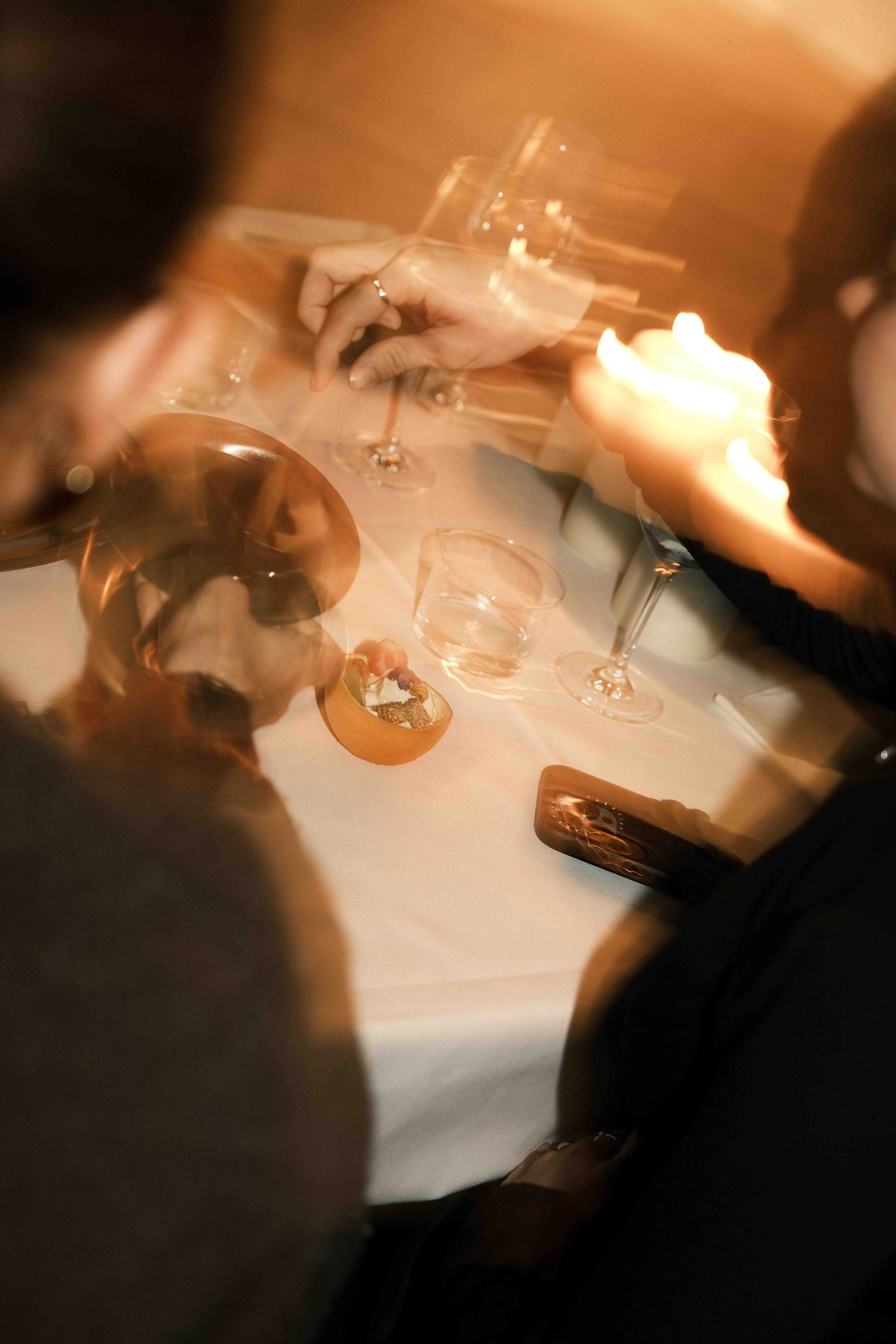 Menschen sitzen an einem Tisch mit Gläsern und Kerzenlicht, es entsteht eine Bewegungsunschärfe.