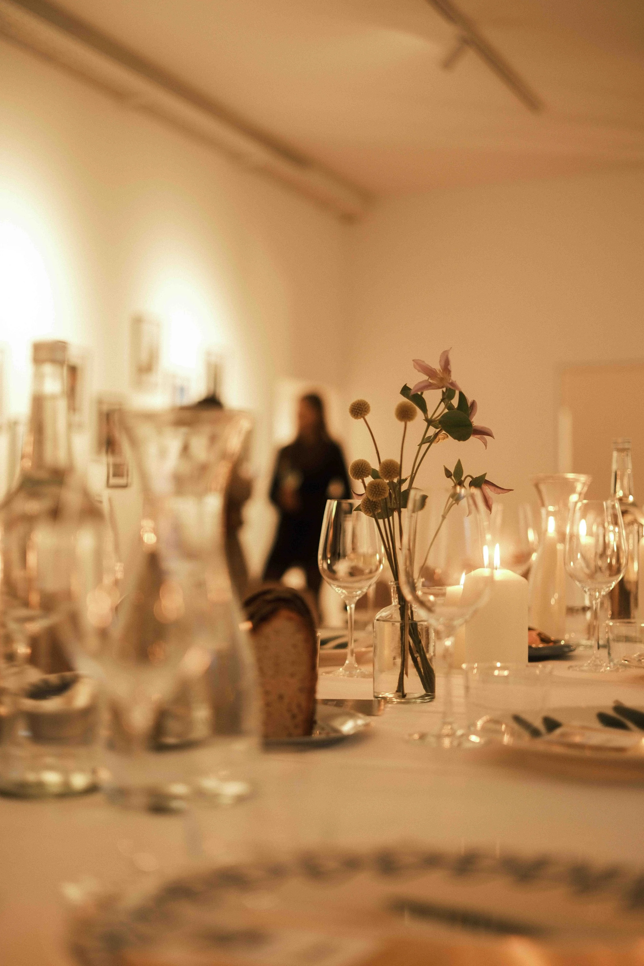 Ein Tisch mit Kerzen, Glaswaren, einer Blumenvasen mit Blumen und gedecktem Geschirr bei einer eleganten Veranstaltung.