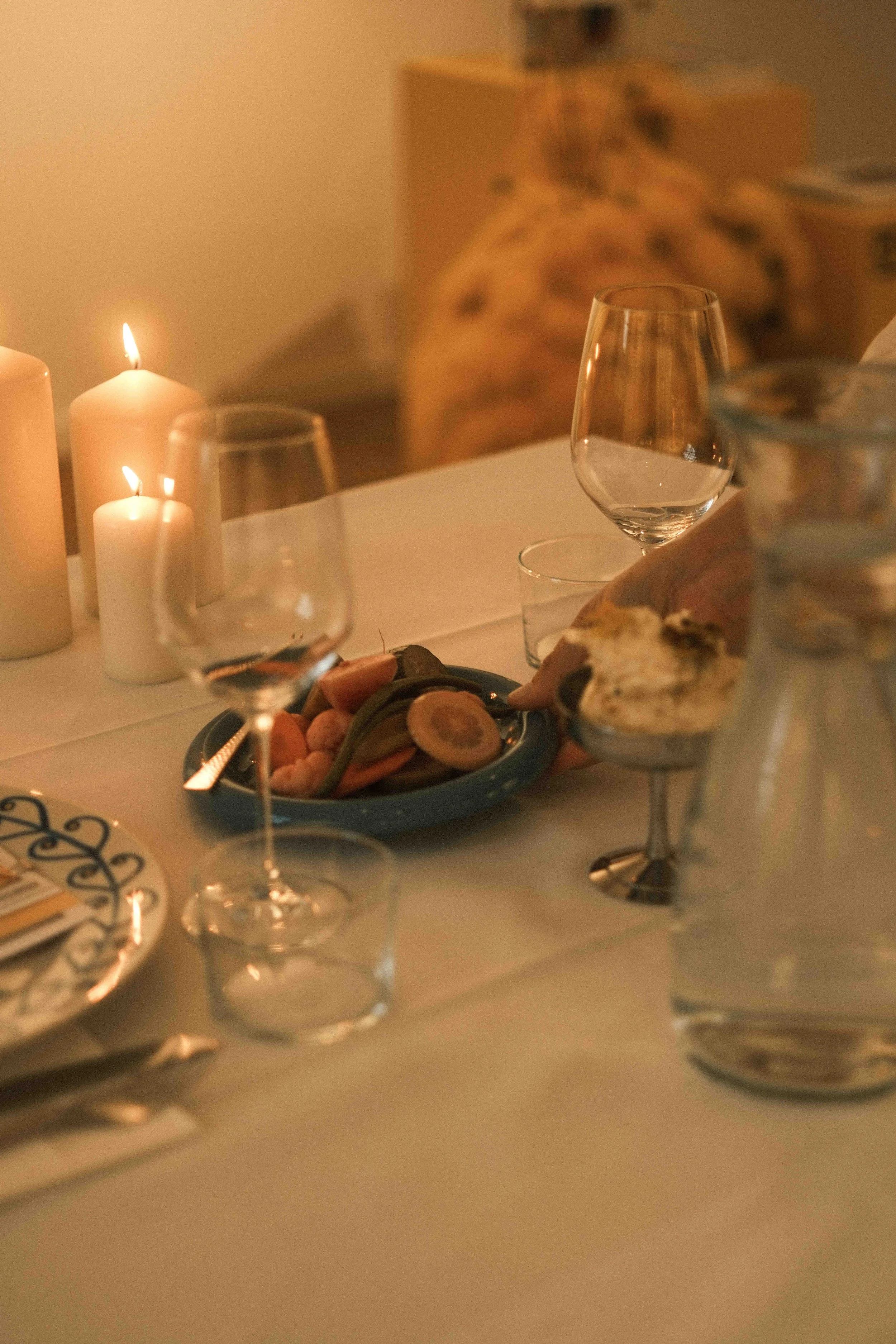 Ein festlich gedeckter Esstisch mit Kerzen, Weingläser, einem Teller mit Scheiben von Zitrusfrüchten und einem Kuchen oder Gebäck. Im Hintergrund eine verstaubte Atmosphäre.