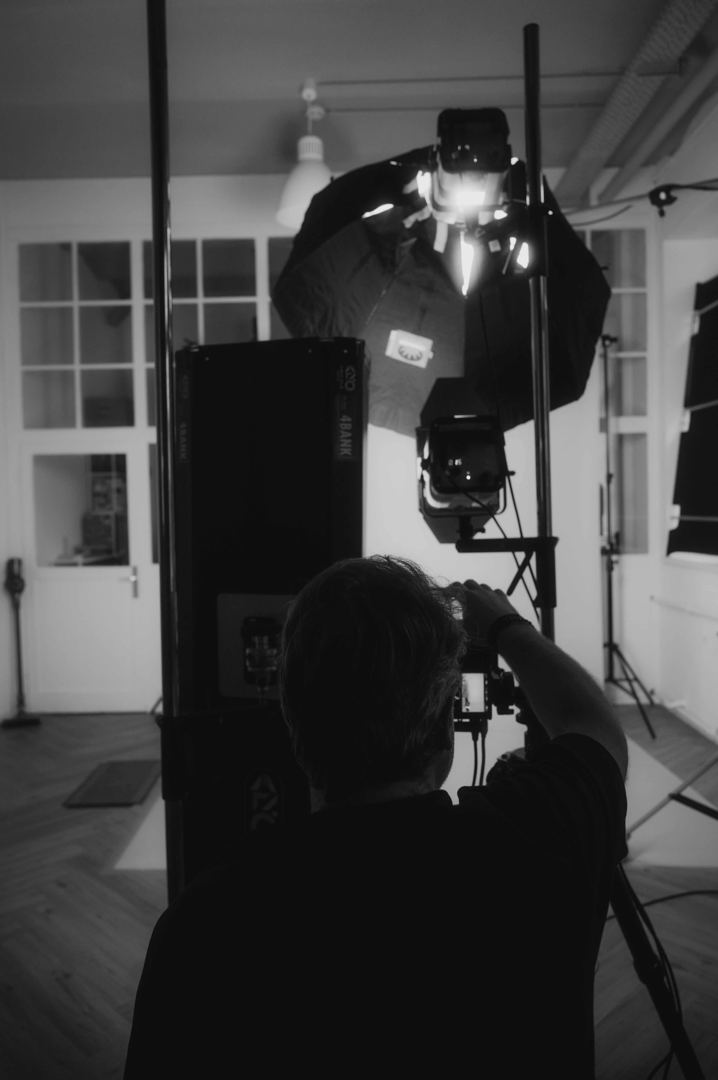 Ein Fotograf beim Fotoshooting im Studio, aufgenommen in Schwarz-Weiß, mit professionellem Kameraequipment und Beleuchtung.