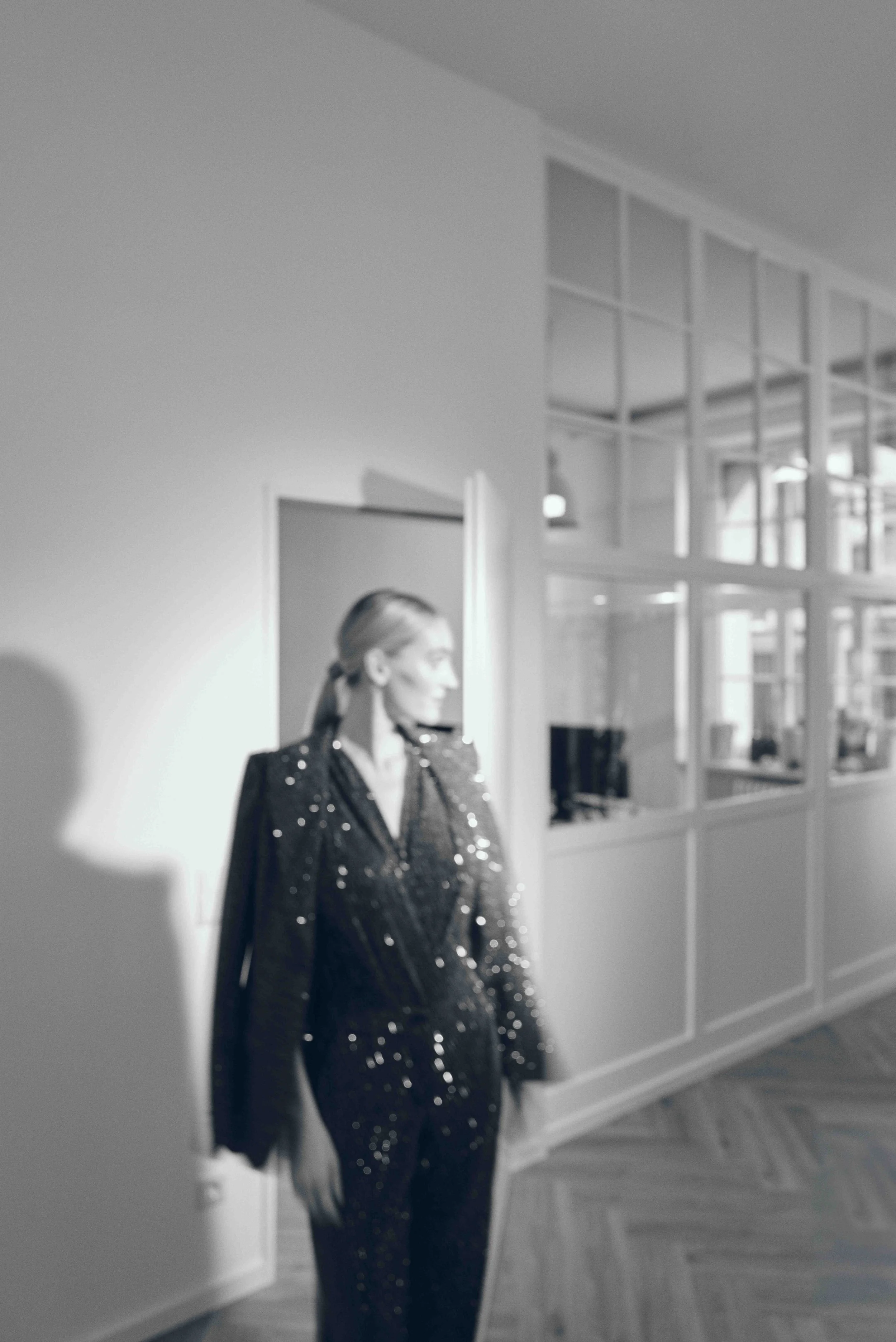 Frau in glitzernder schwarzer Jacke in einem modernen Büro oder Konferenzraum, die an der Wand steht.