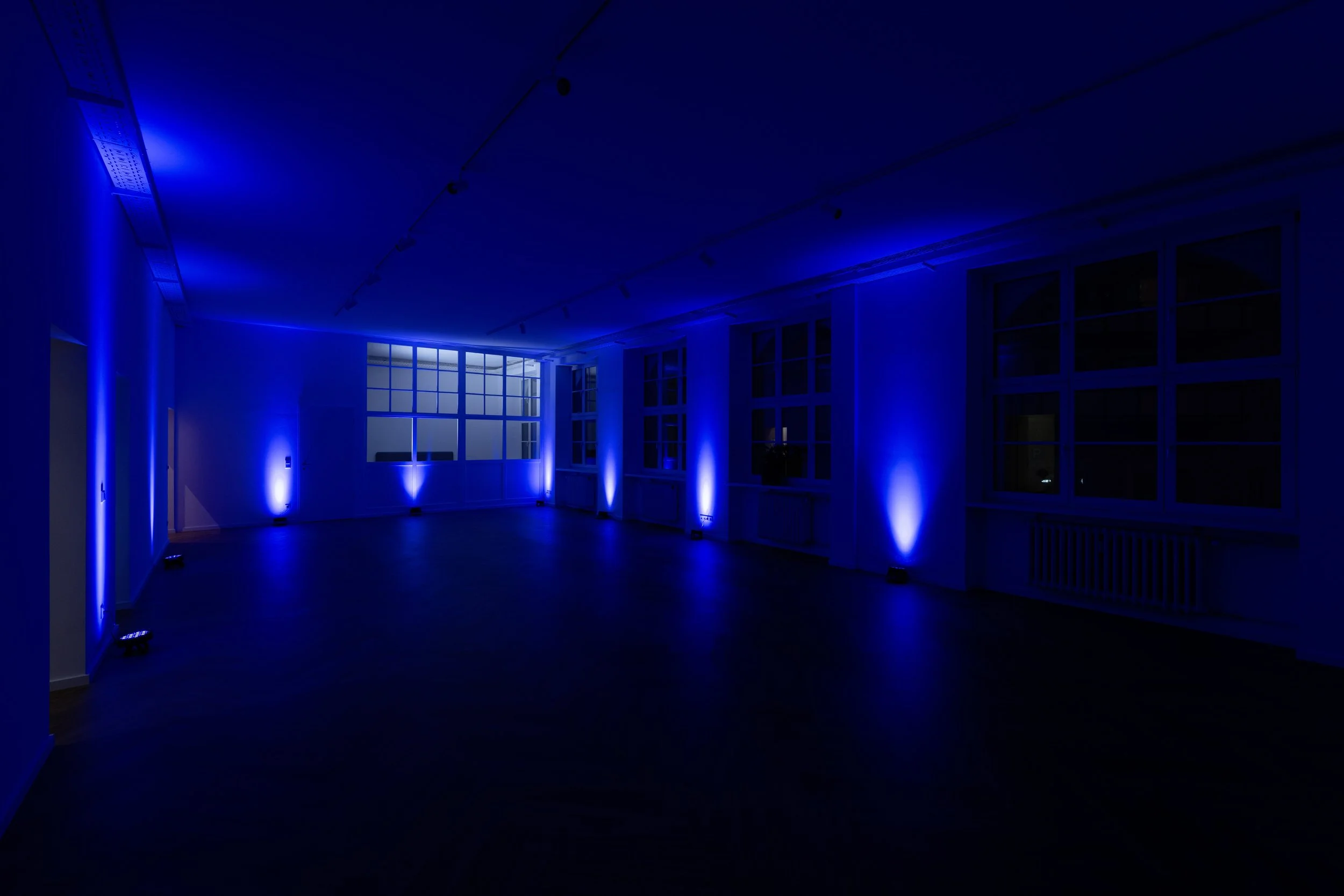 Leerer Raum mit blauer Beleuchtung und großen Fenstern in der Nacht.