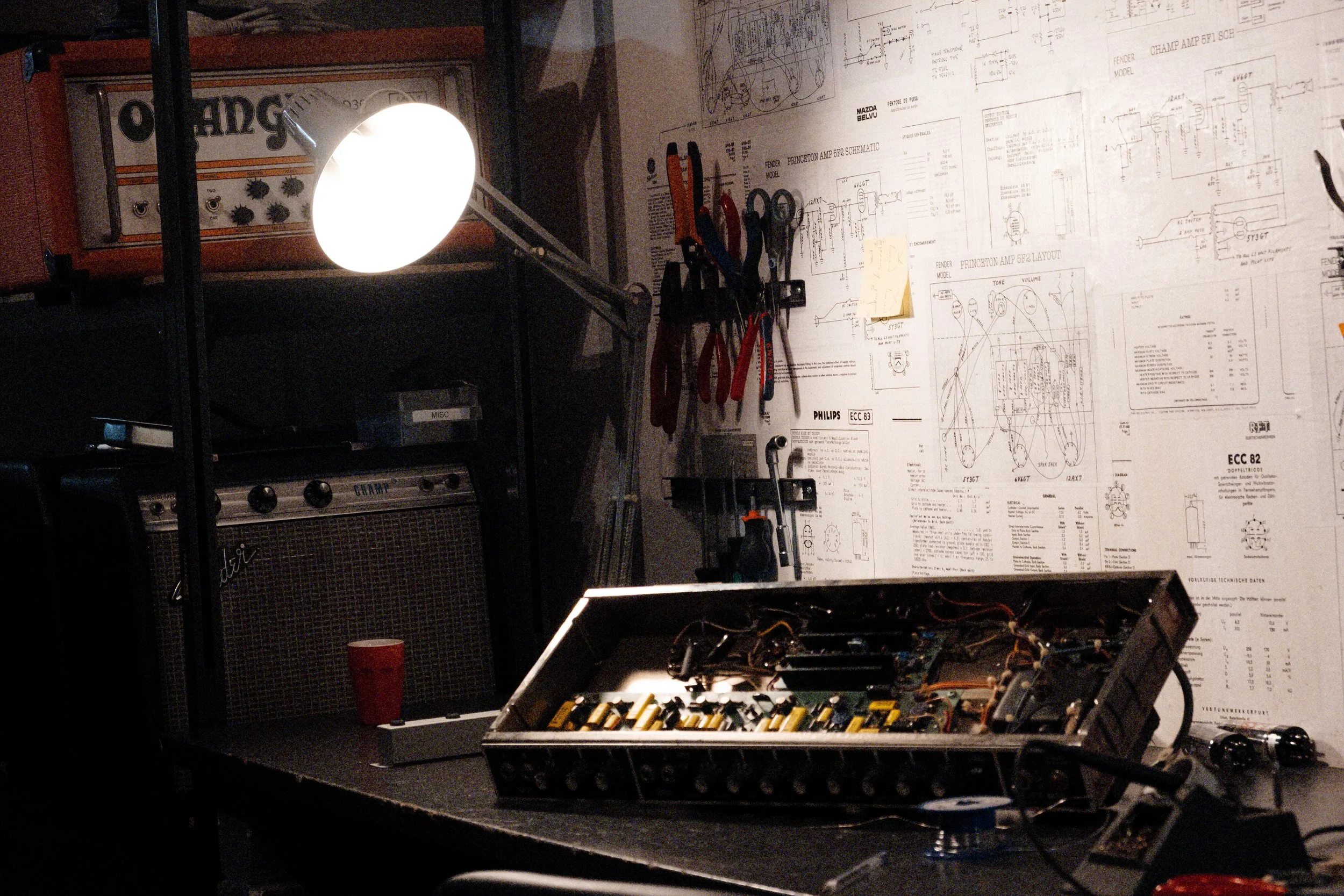 Travail sur le châssis d’un ampli à lampes dans l’atelier, schémas techniques en arrière-plan