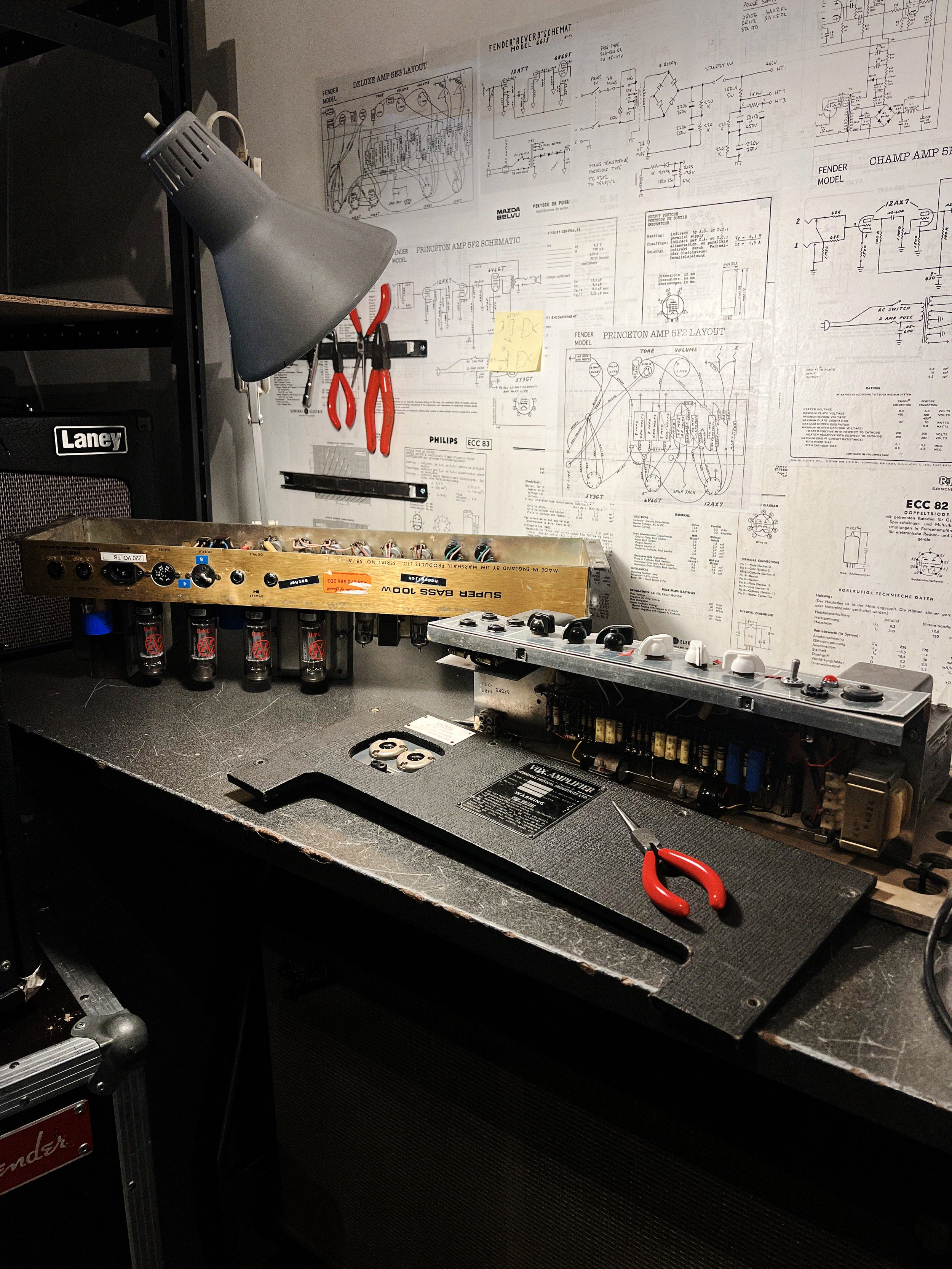 Un poste de travail avec deux amplis vintage ( un Vox Ac 50 et un Marshall) , des outils et des schémas annotés en arrière-plan.