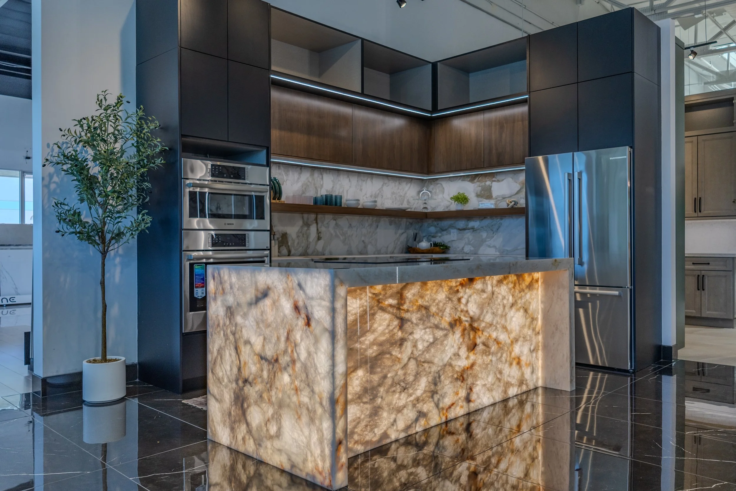 Modern kitchen with onyx island, black cabinets, stainless steel fridge, built-in oven, and marble backsplash.