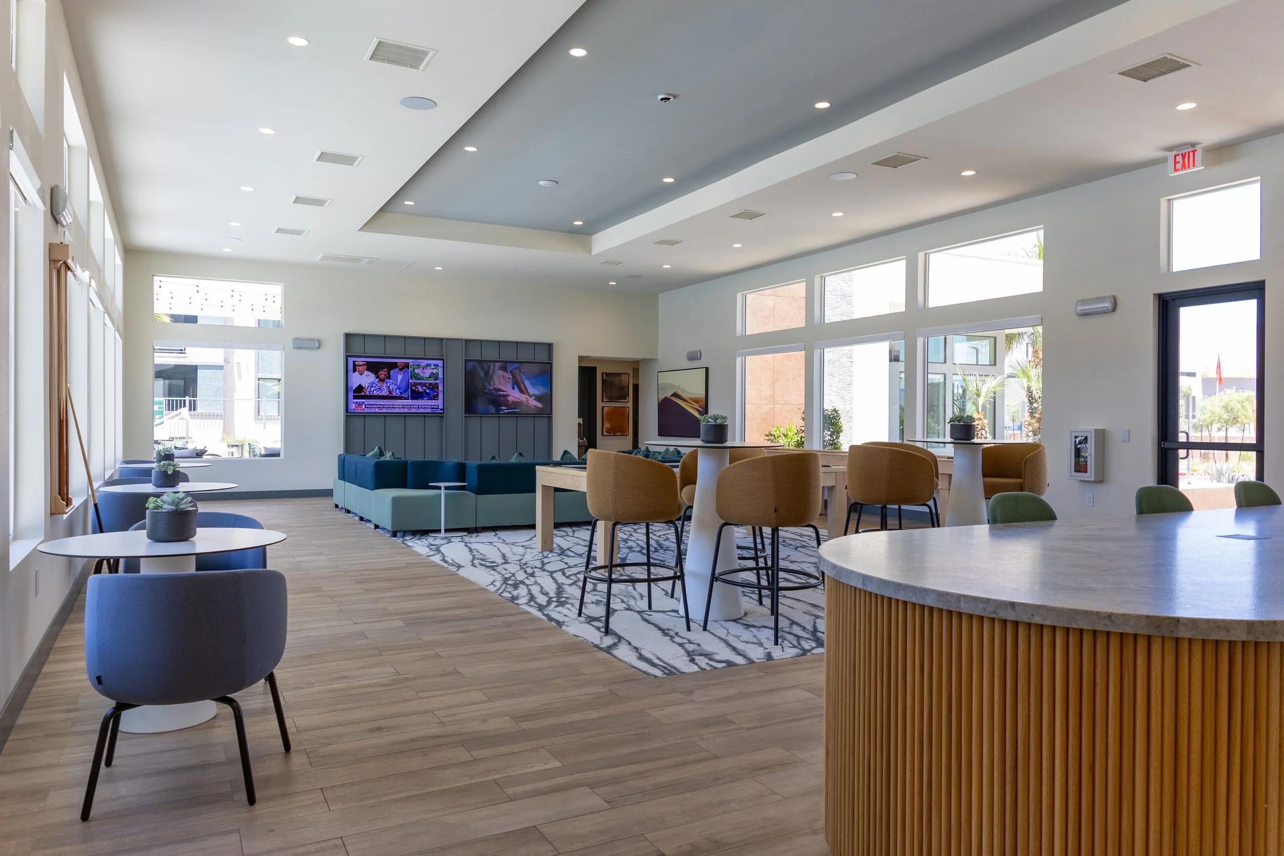 Modern lounge area with colorful chairs, sofas, a television, and large windows letting in natural light.