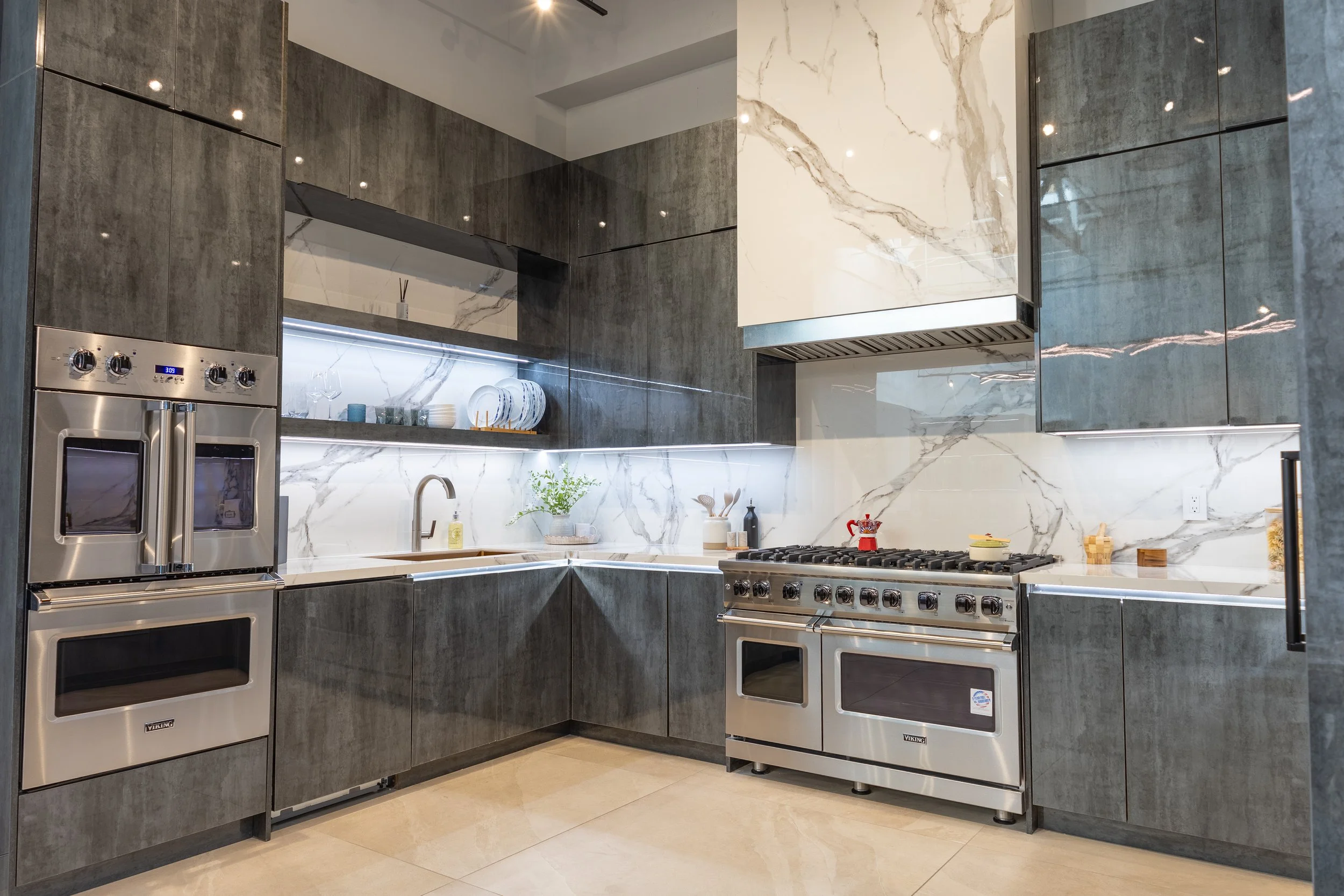 Modern kitchen with stainless steel appliances, gray cabinetry, marble backsplash, and a window with dishes and decor.