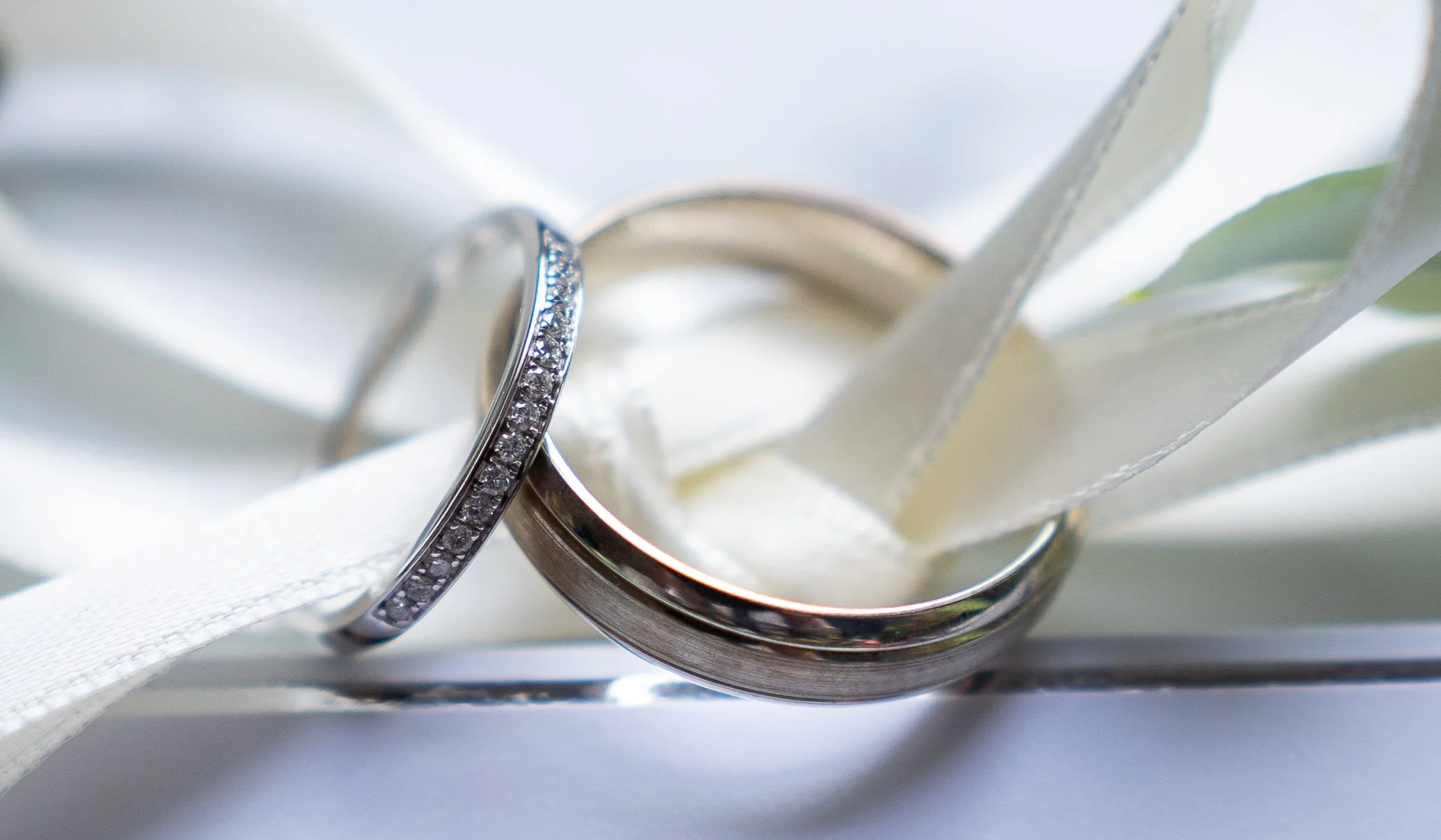 Close-up image of two wedding rings resting on white satin fabric, with one ring decorated with small diamonds.