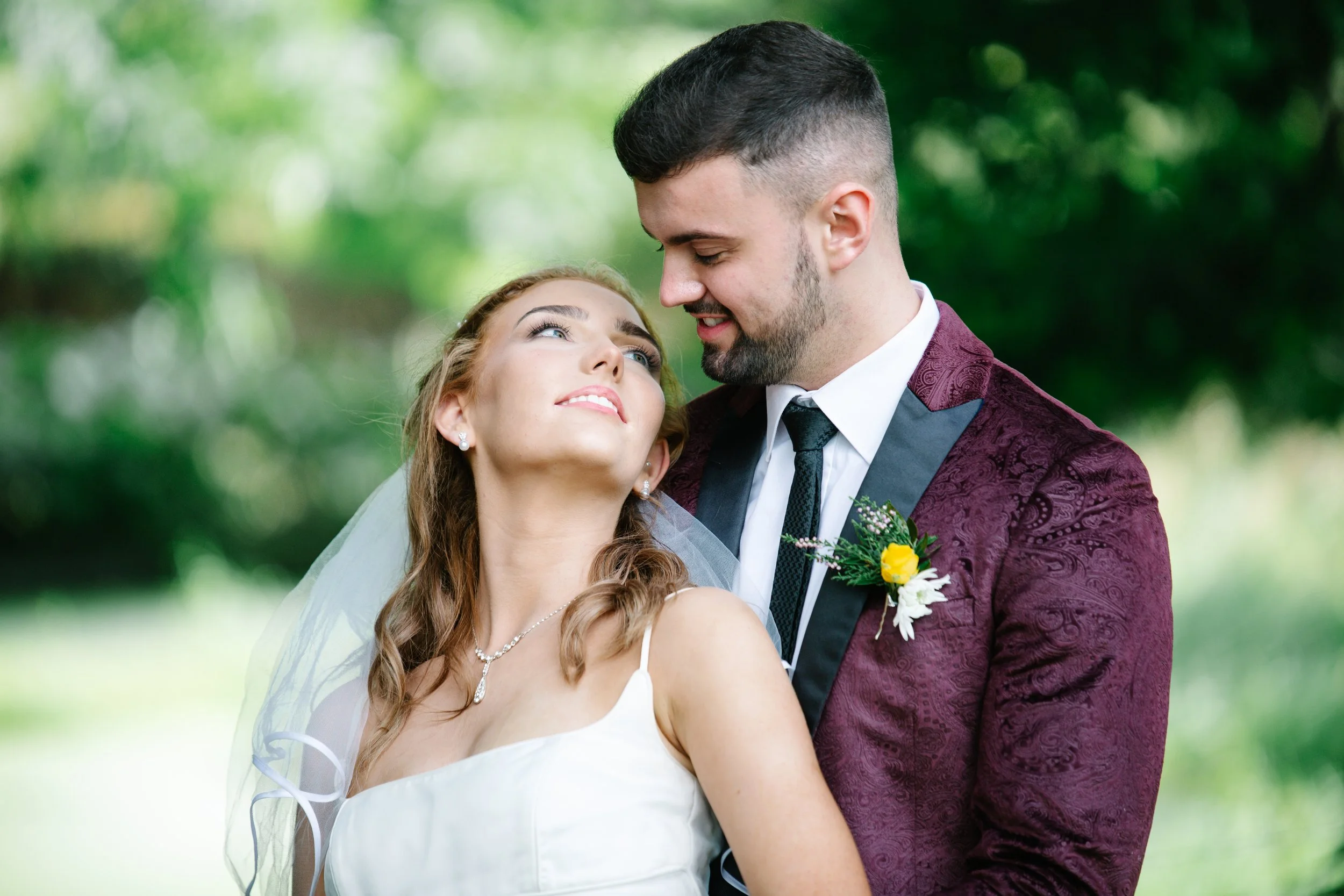 A bride and groom descending outdoor stairs, smiling and holding drinks, during a wedding celebration amid wooden and brick structures.