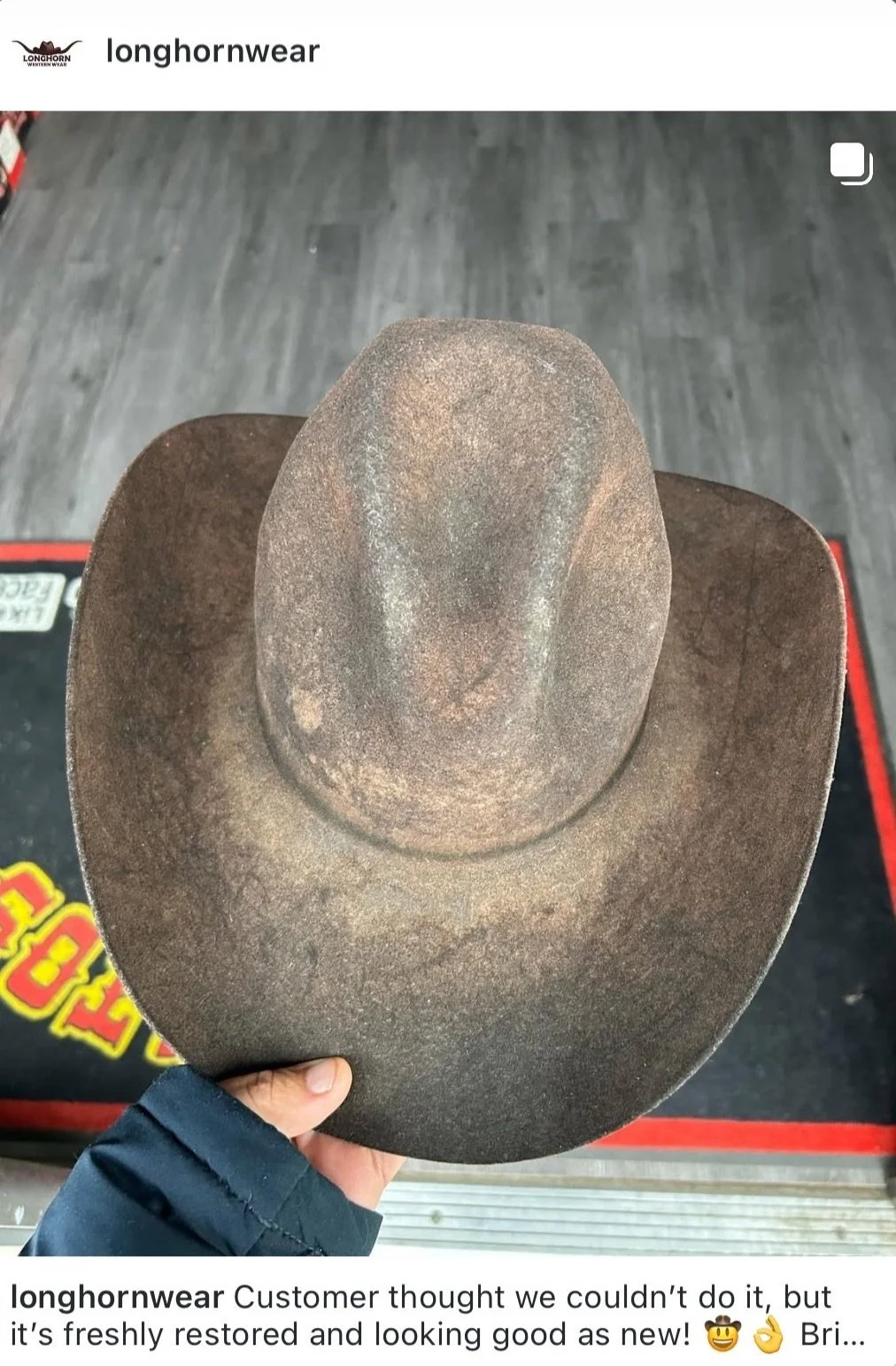 A weathered, vintage cowboy hat with a high crown and wide brim, being held by a person wearing a dark jacket.