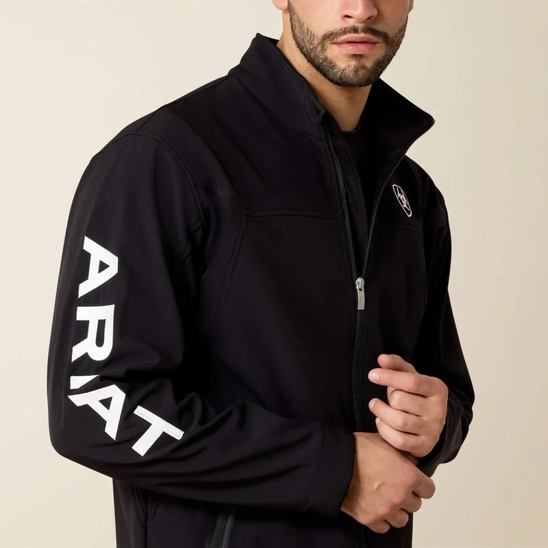 Close-up of a man wearing a black jacket with a high collar, zippered front, and white text reading 'PRYTAT' on the sleeve, against a plain background.