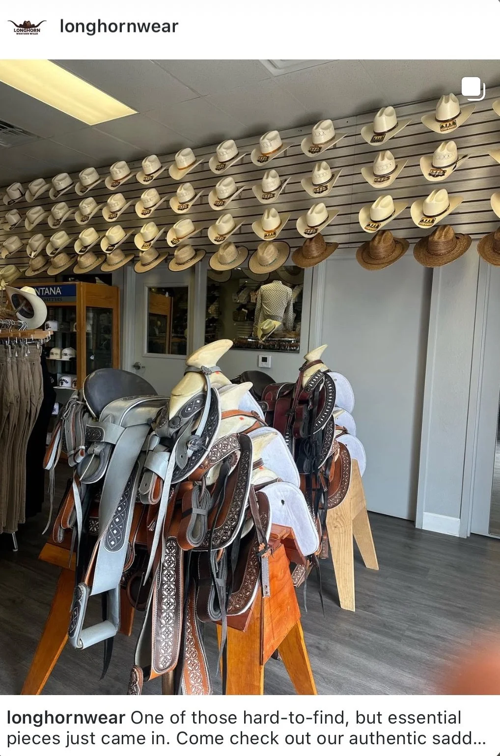A wall display of various cowboy hats in different colors and styles, along with a table of saddles with intricate designs, in a Western clothing store.