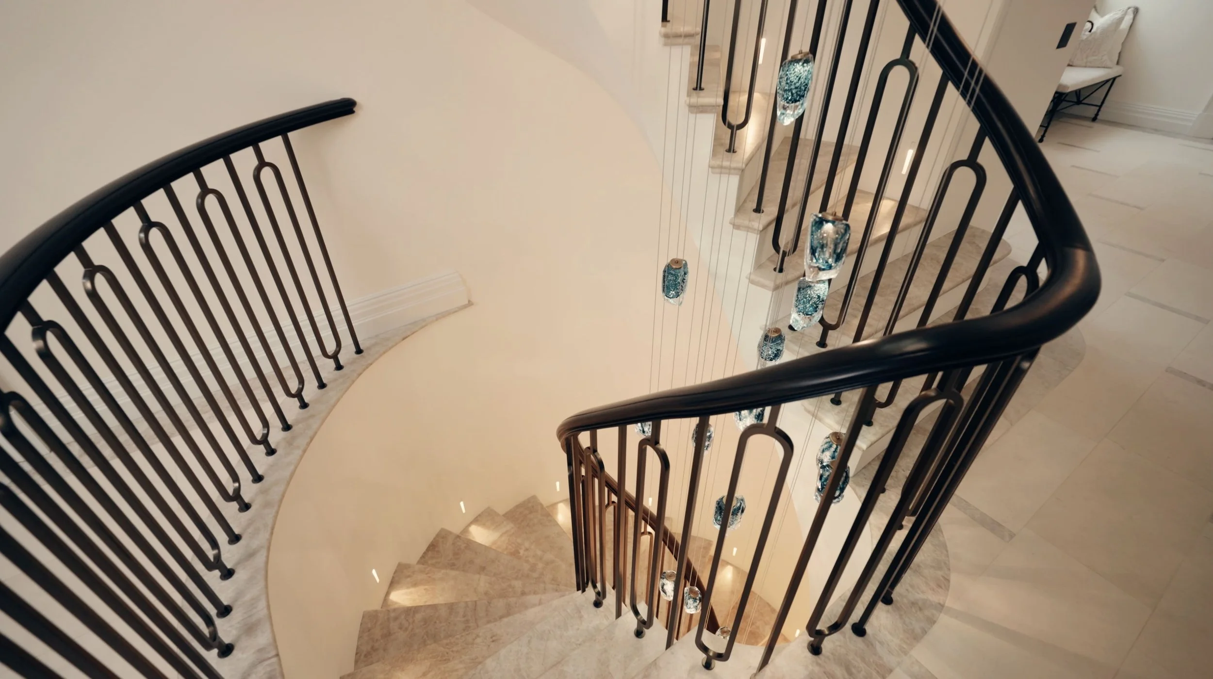 Looking down a staircase with black metal railing and beige marble steps, decorated with hanging glass and metal lanterns, in a modern home interior.