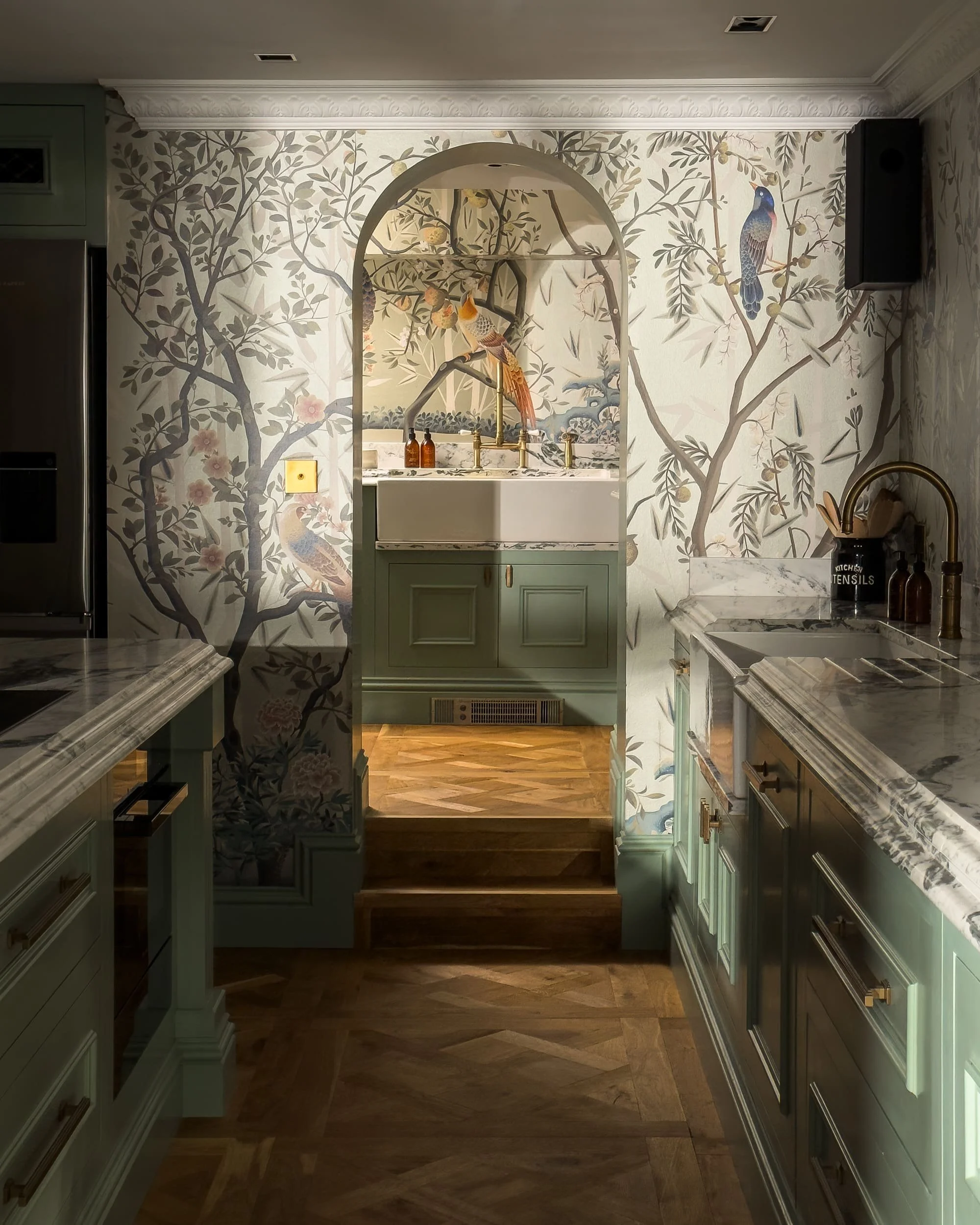A kitchen featuring green cabinetry, marble countertops, and a decorative wallpaper with birds and trees.