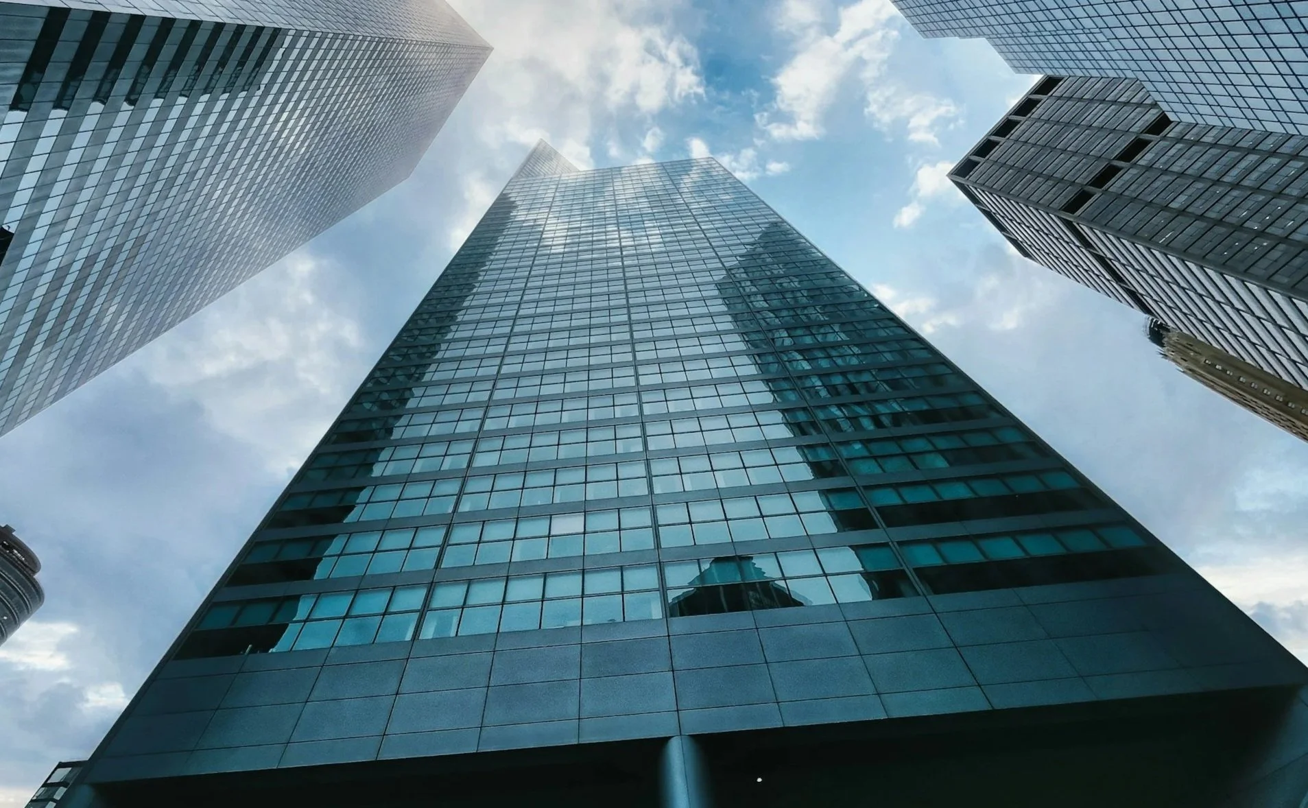 Low-angle view of modern glass skyscrapers against a partly cloudy sky.