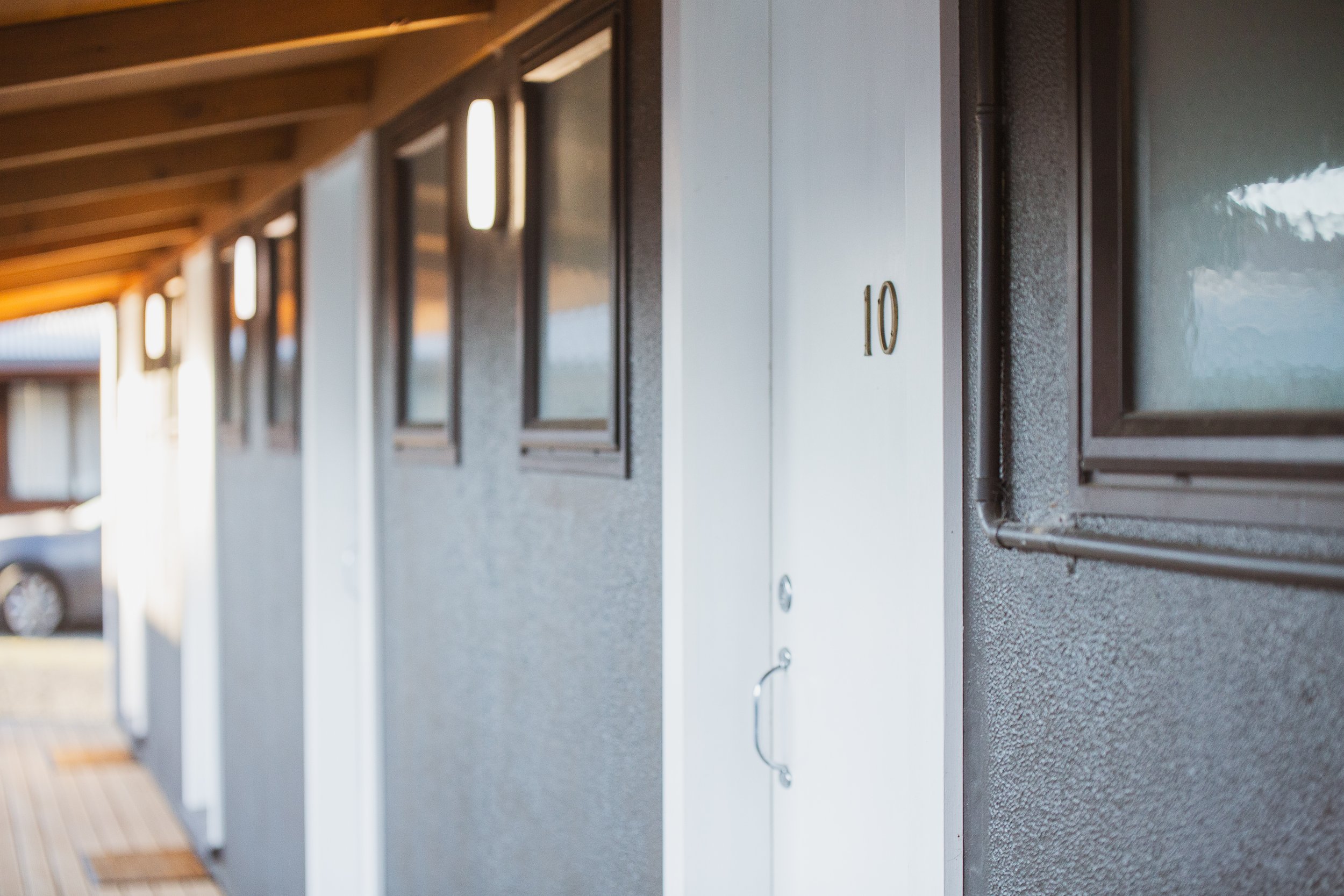 Exterior view of a hotel corridor showing a door with the number 10, multiple windows, and cars parked outside.