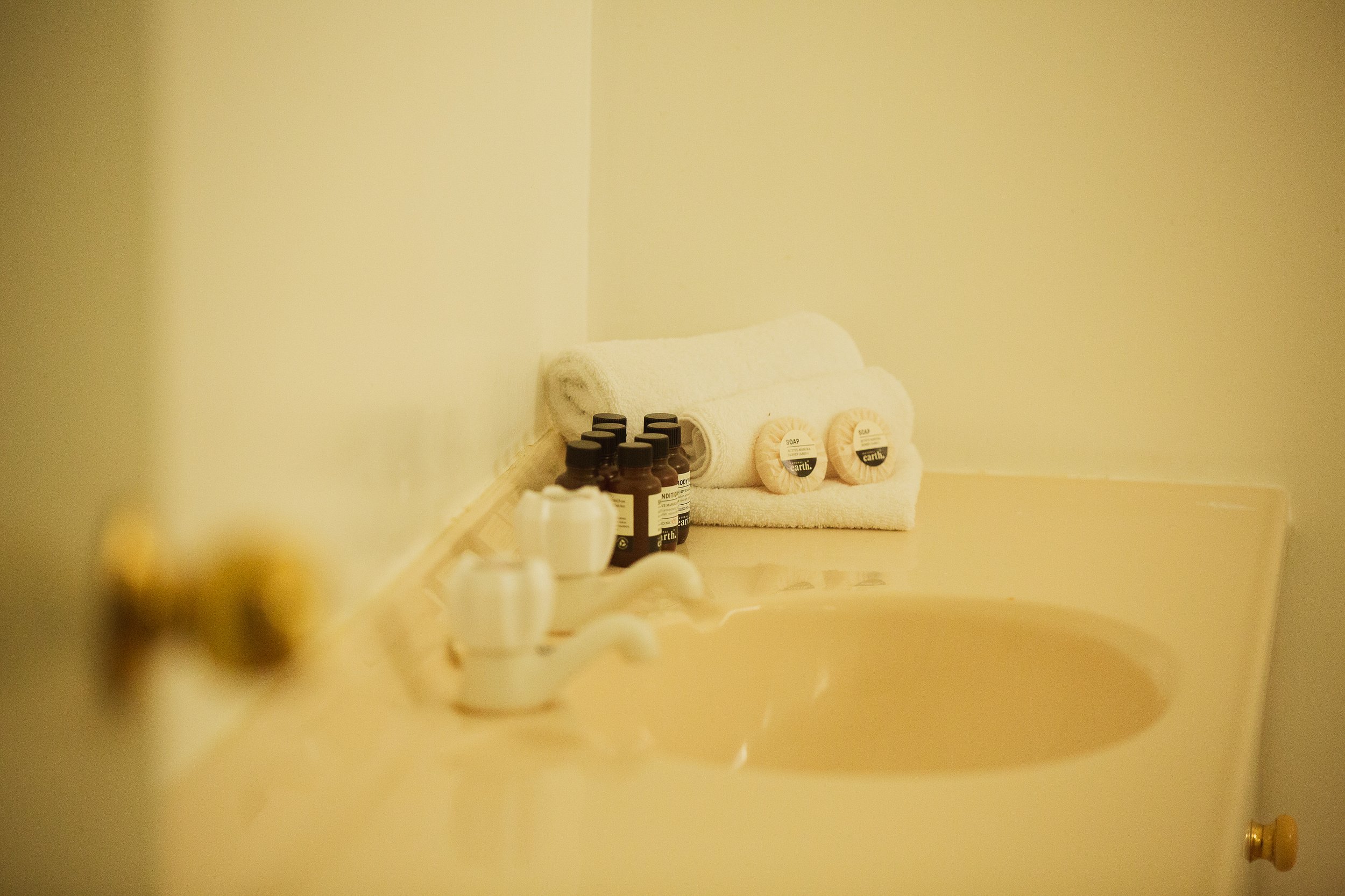 Bathroom countertop with neatly rolled white towels, small bottles, and soap bars.