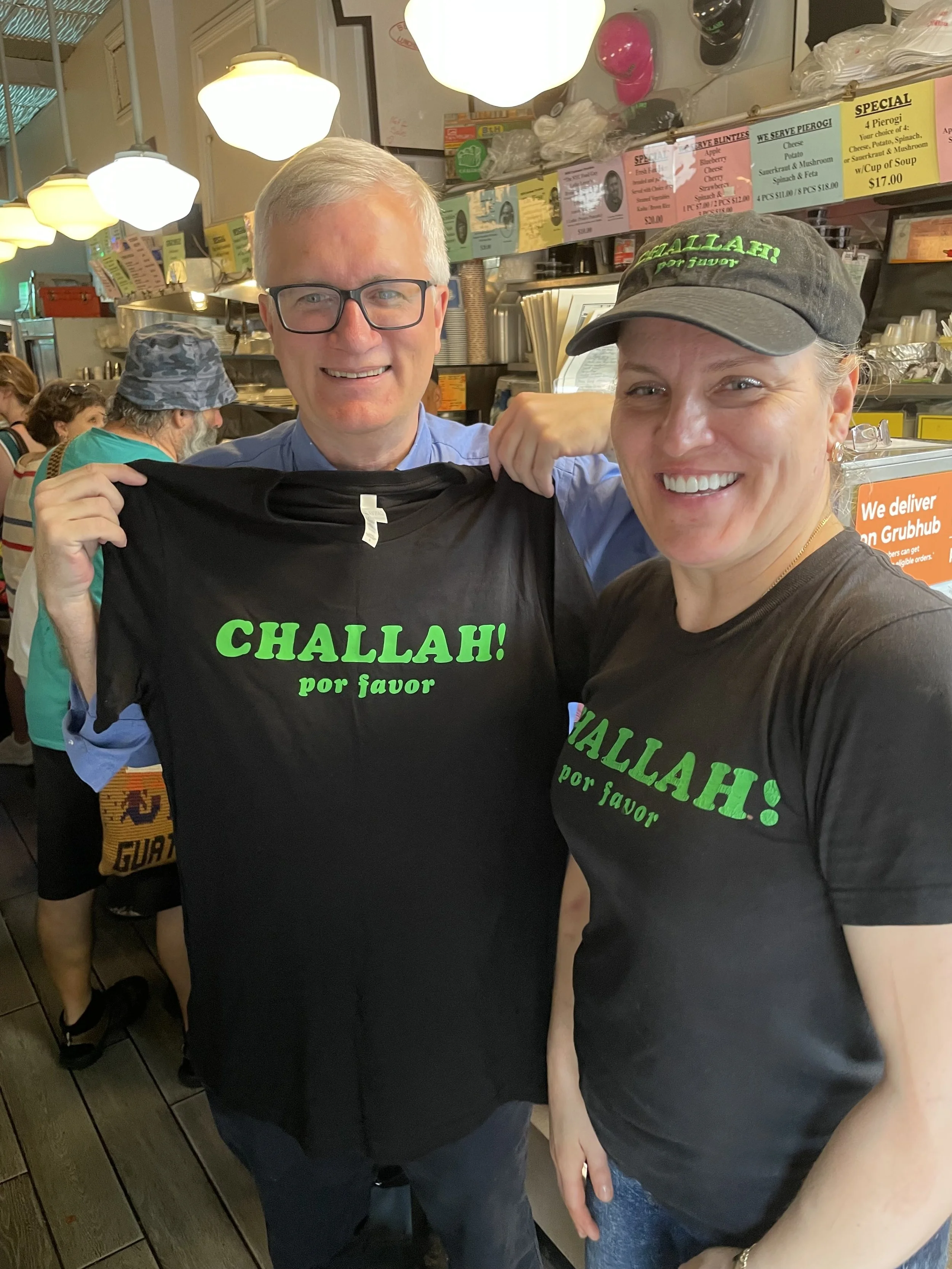 Senator-Brian-Kavanagh-with-BH-owner-Ola-holding-challah-por-favor-Tshirts-in-front-of-counter.jpeg