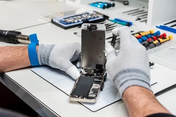 Person repairing a disassembled smartphone at a workbench with tools and equipment.