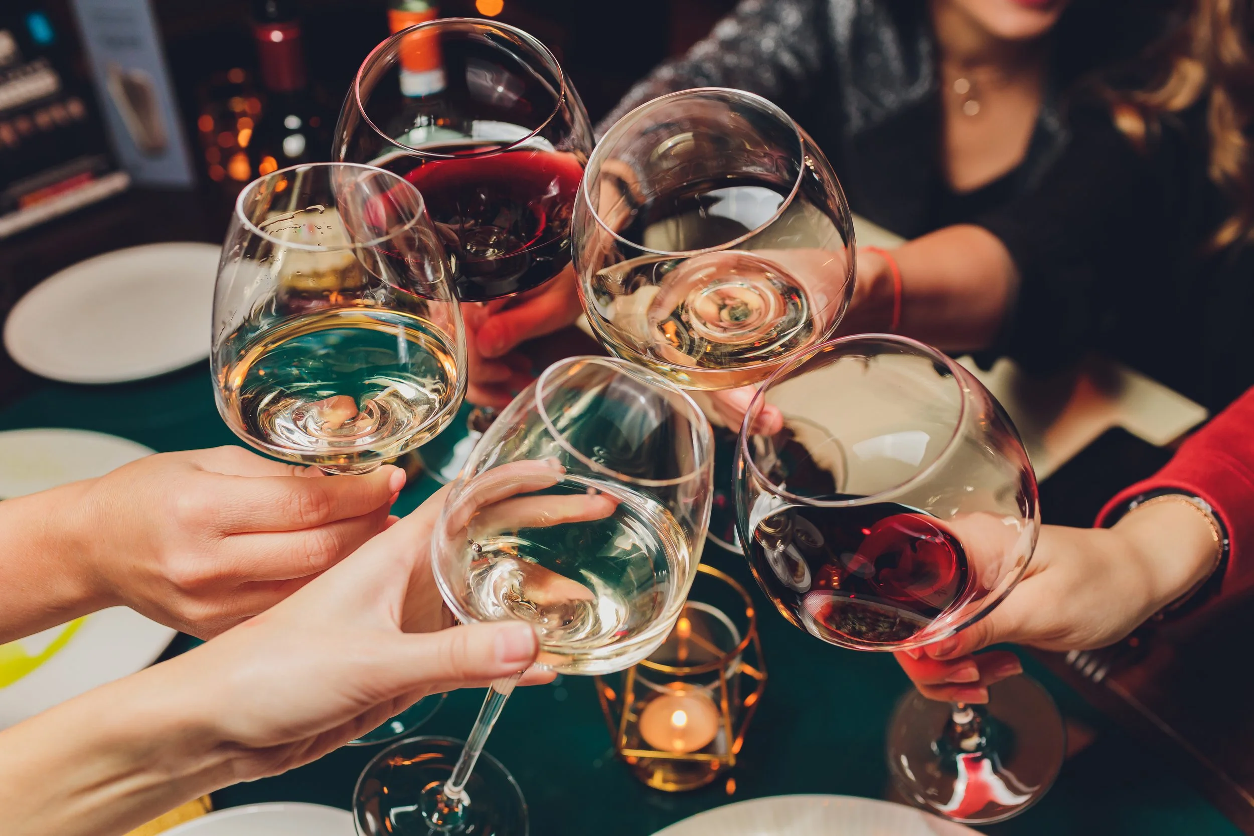 Group of people celebrating with glasses of white and red wine at a dinner table.