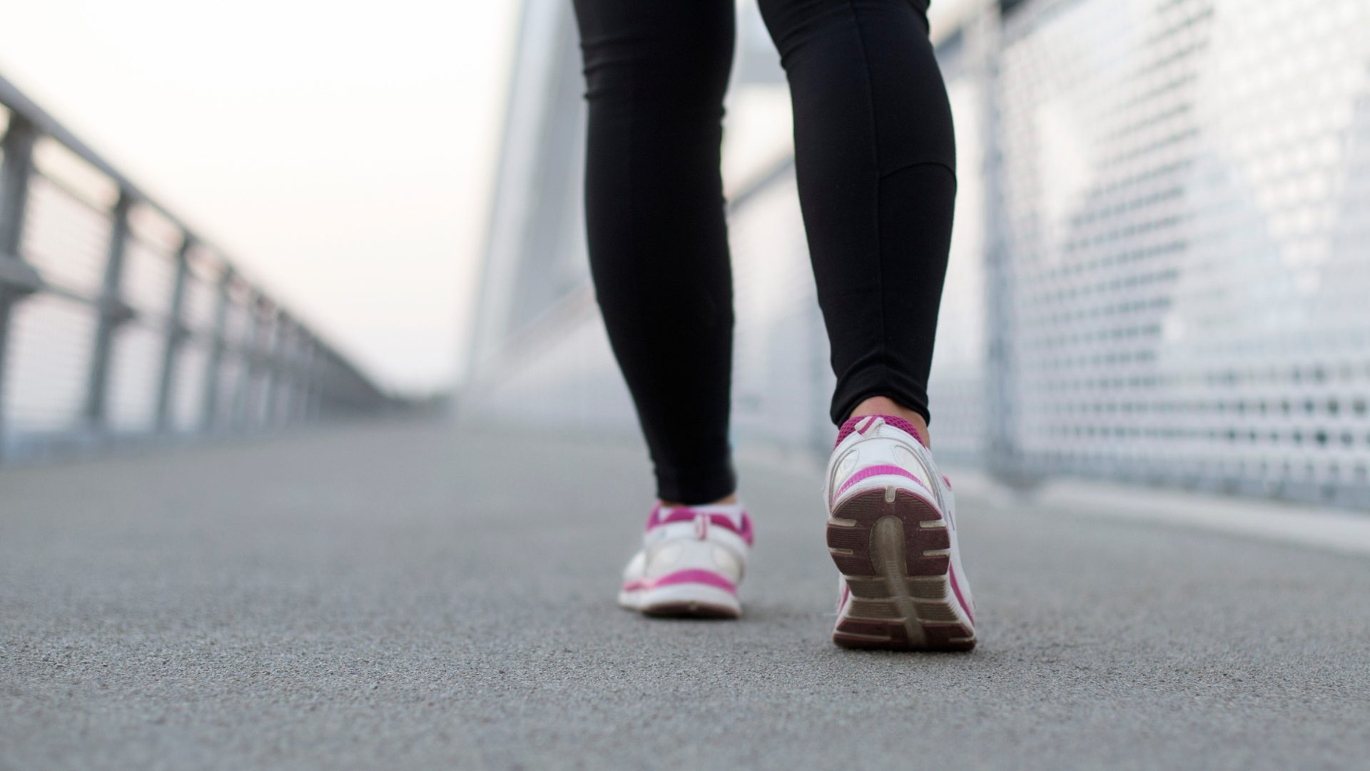 Close-up of a person walking on a bridge in athletic shoes and black leggings