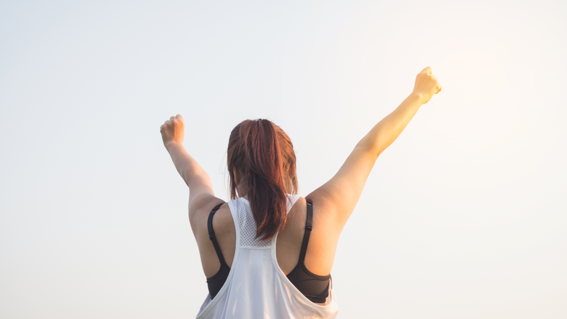 Person with red hair raising both arms in victory against a pale sky