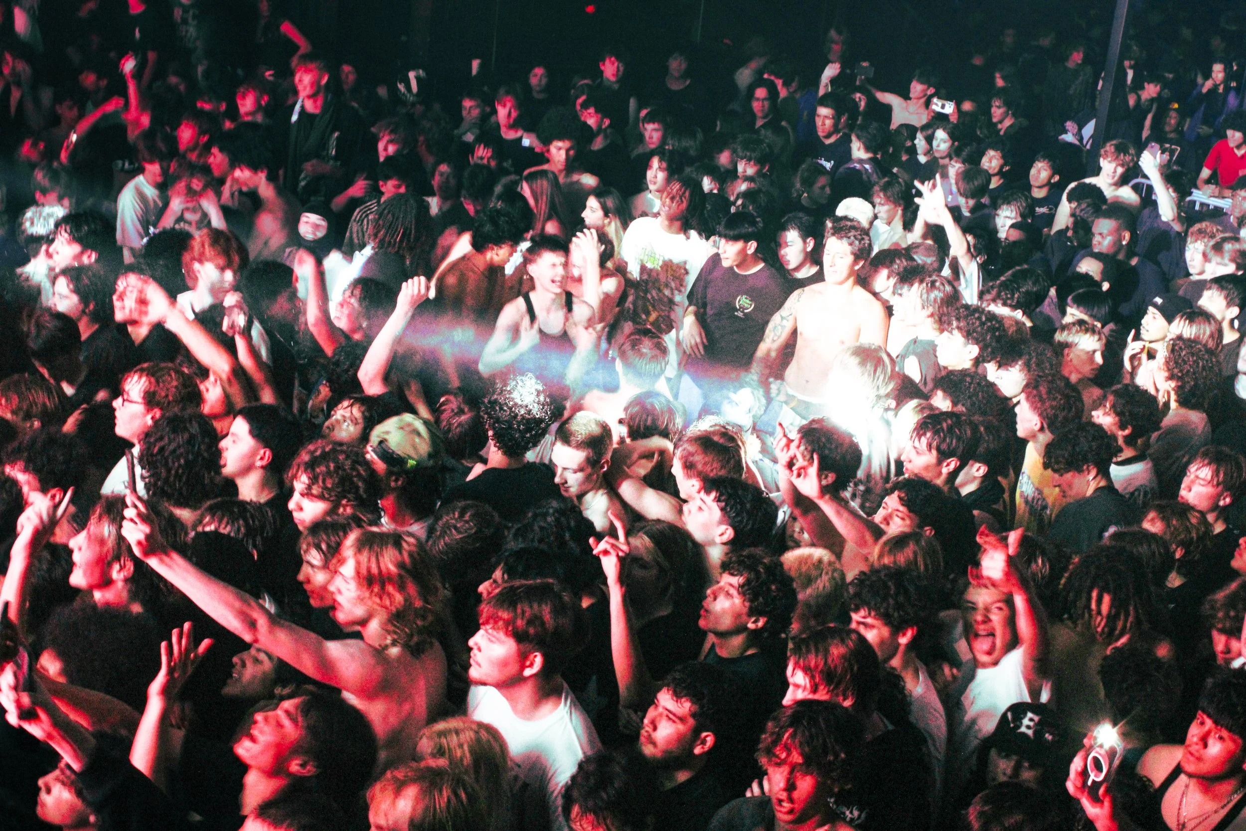 Crowd at a concert or dance party, dancing and enjoying music. People are close together, some raising their hands and smiling.