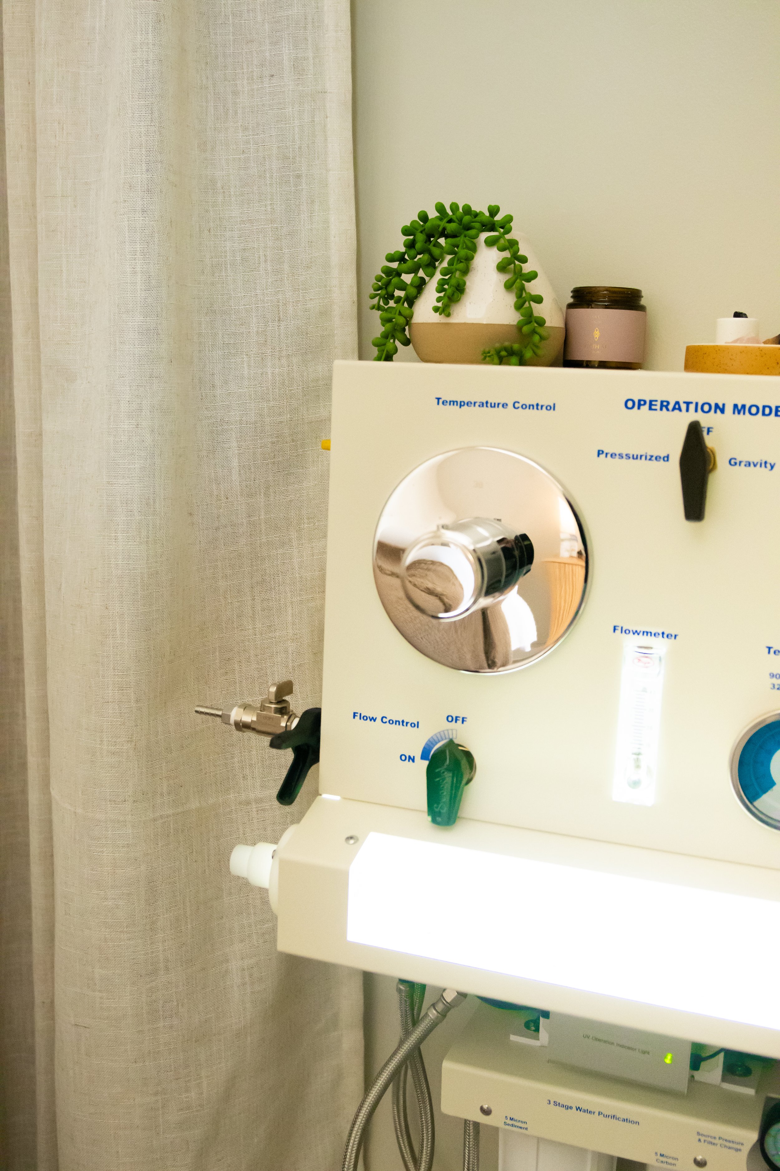 Medical device with control dials and a flow control switch, situated next to a beige curtain, with decorative items including a small succulent plant and jars on top.
