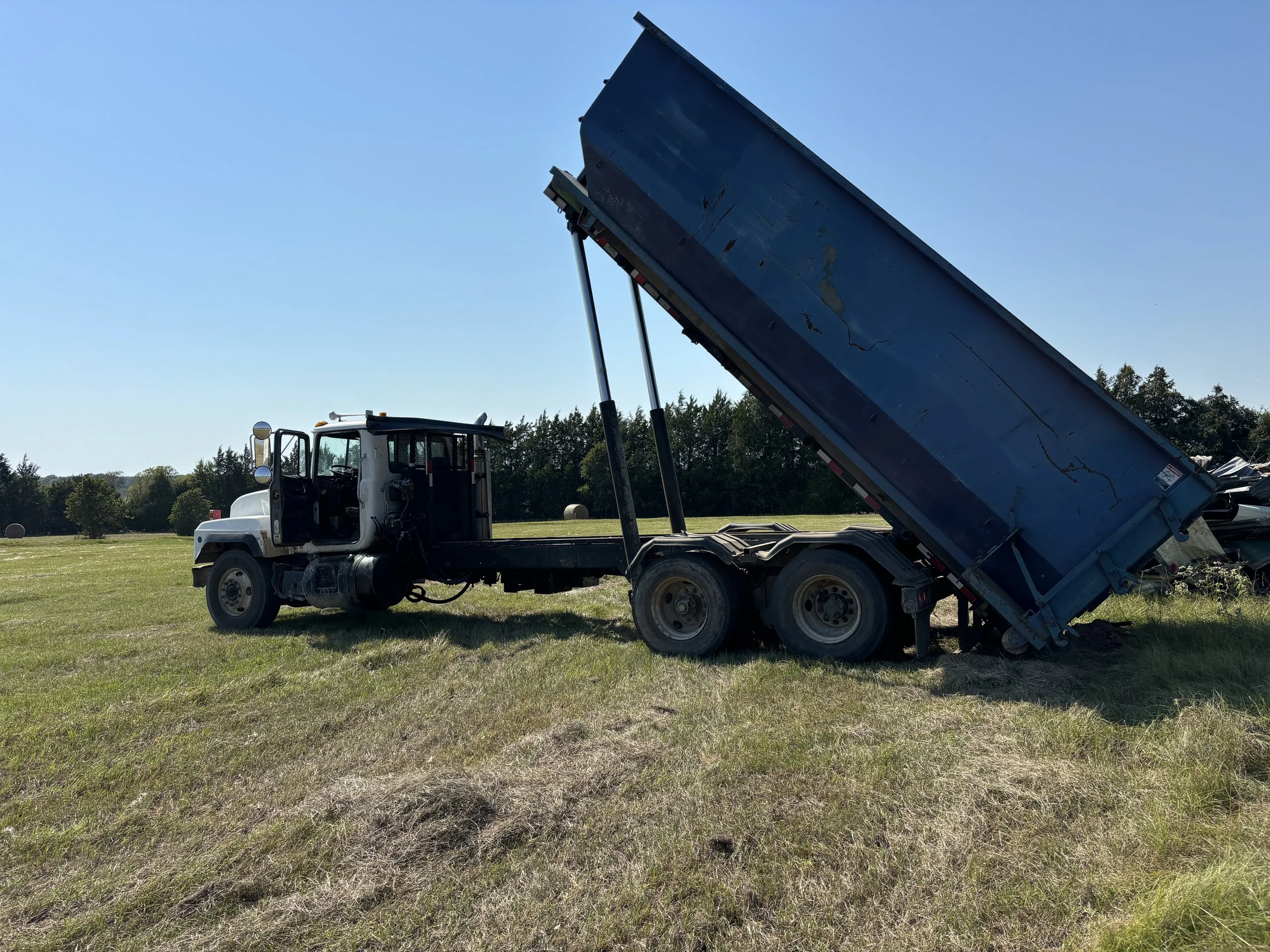A dump truck with its bed raised, parked on a grassy field on a sunny day.