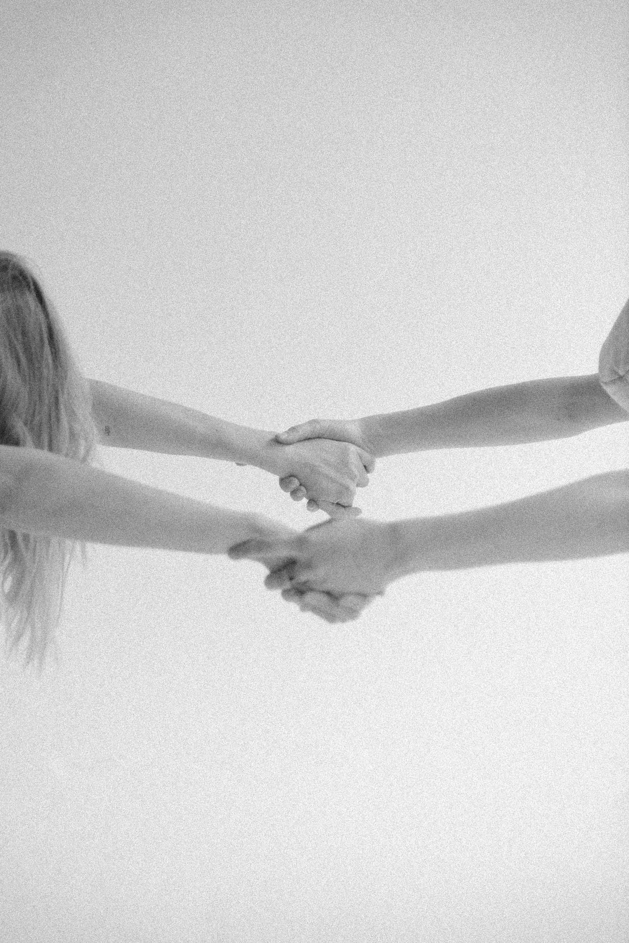 Two people shaking hands, facing each other, with their arms extended toward the center of the image. Black and white photo