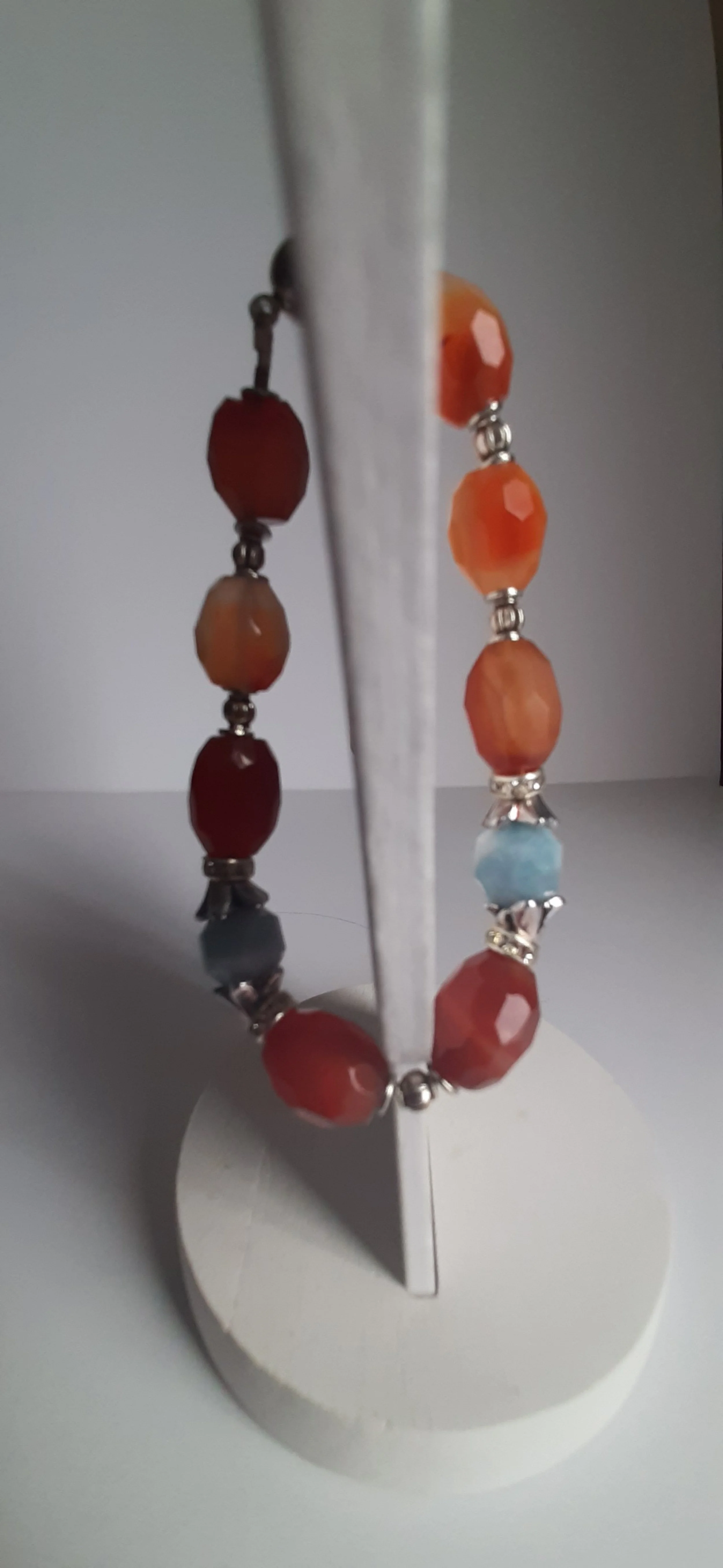 Colorful beaded bracelet displayed on a white stand, with beads in red, orange, blue, and neutral tones.